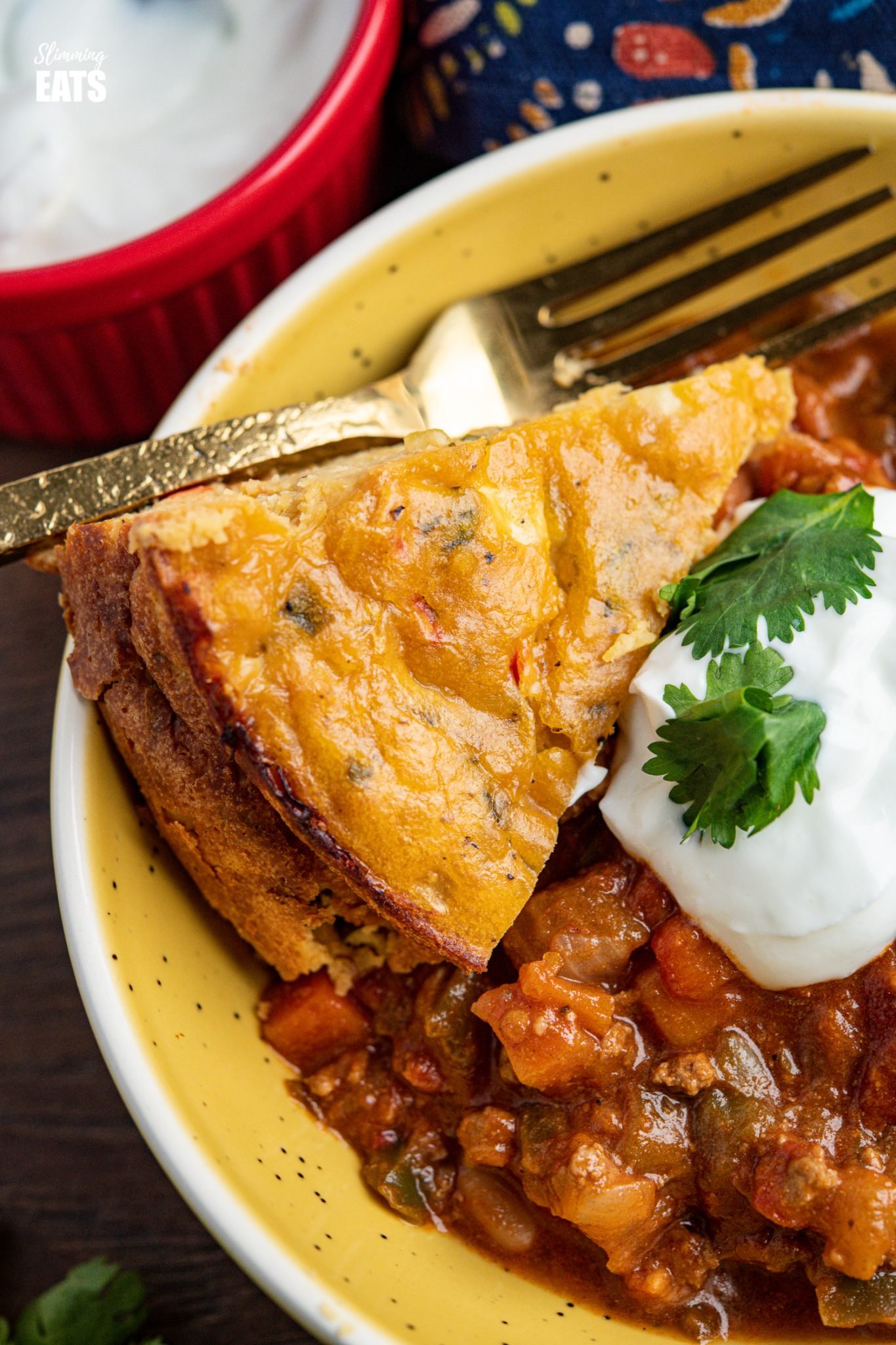 close up of lentil cheddar bake in yellow bowl with chilli and sour cream