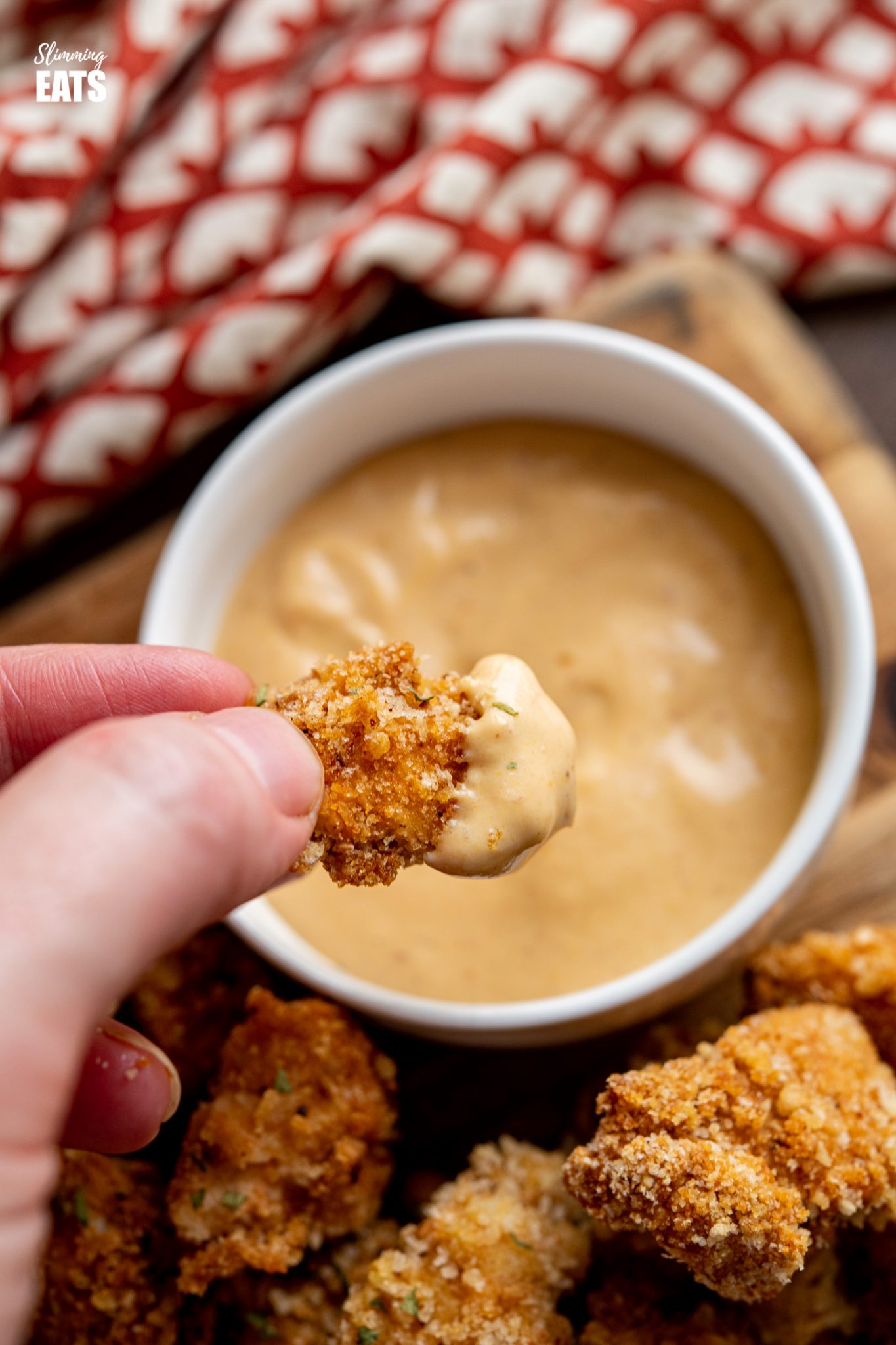 hand dipping popcorn chicken bite into a white bowl with chicken dipping sauce. 