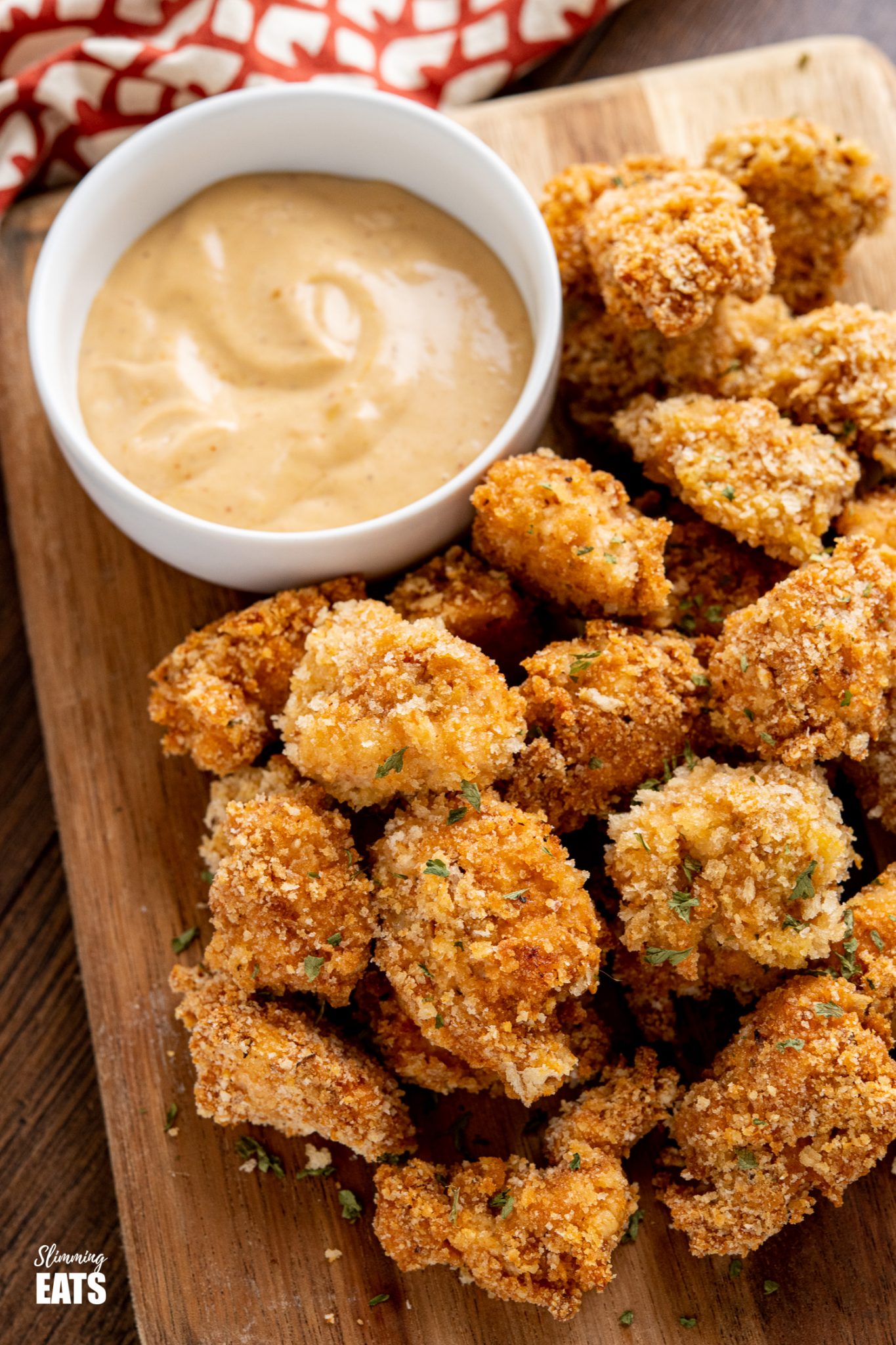 close up of popcorn chicken bites on a wooden board with chicken dipping sauce