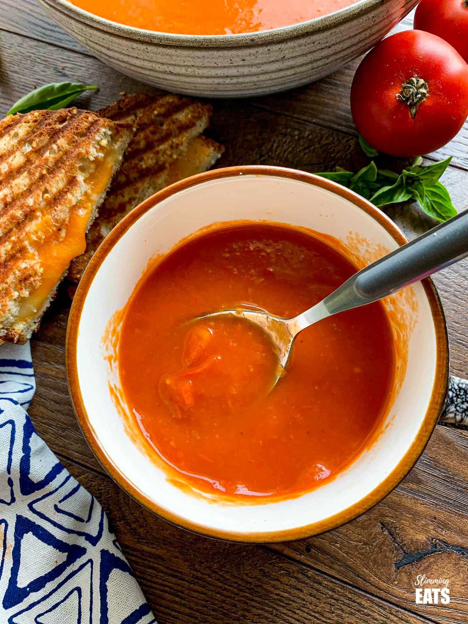 Roasted Red Pepper and Tomato Soup in cup with grilled cheese to the left and tomatoes on the right