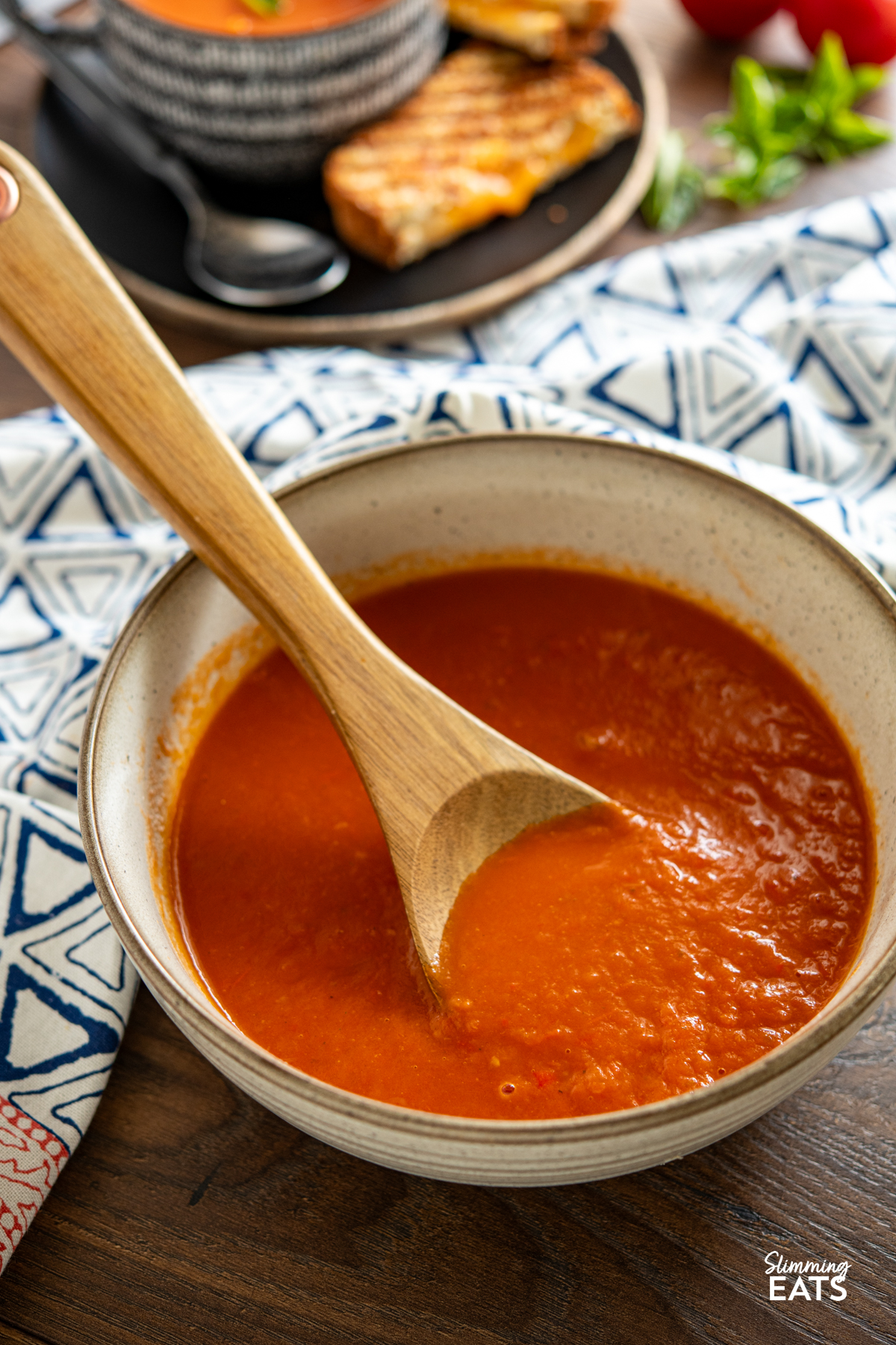 Roasted Red Pepper and Tomato Soup - a simple but delicious soup made with fresh peppers and tomatoes perfect with a grilled cheese sandwich. Gluten Free, Dairy Free, Vegan, Vegetarian, Slimming Eats and Weight Watchers friendly large speckled brown bowl of roasted pepper and tomato soup with wooden spoon