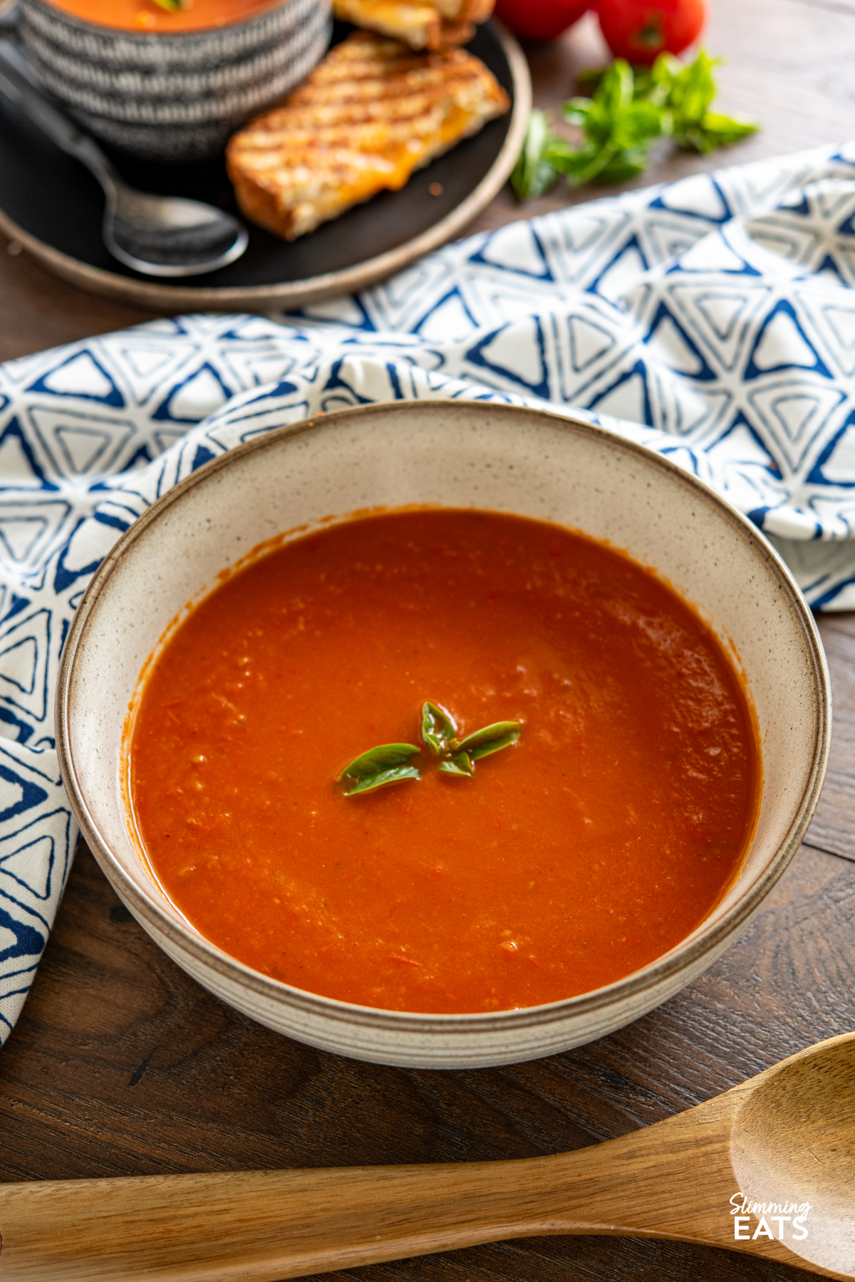 Roasted Red Pepper and Tomato Soup - a simple but delicious soup made with fresh peppers and tomatoes perfect with a grilled cheese sandwich. Gluten Free, Dairy Free, Vegan, Vegetarian, Slimming Eats and Weight Watchers friendly large brown speckled bowl of roasted red pepper and tomato soup with wooden spoon in front