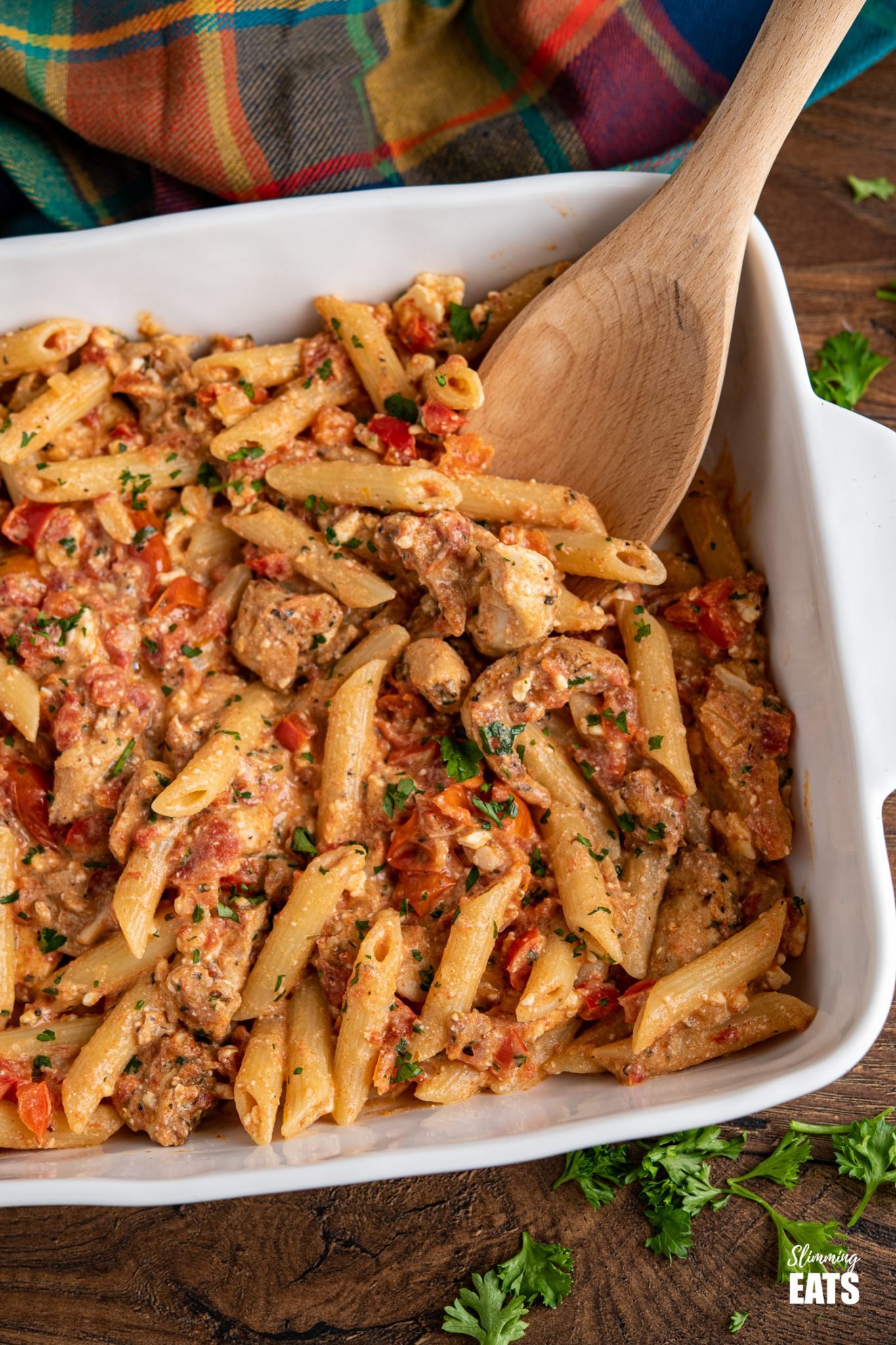 Baked feta pasta in white oven dish with chicken and scattered herbs