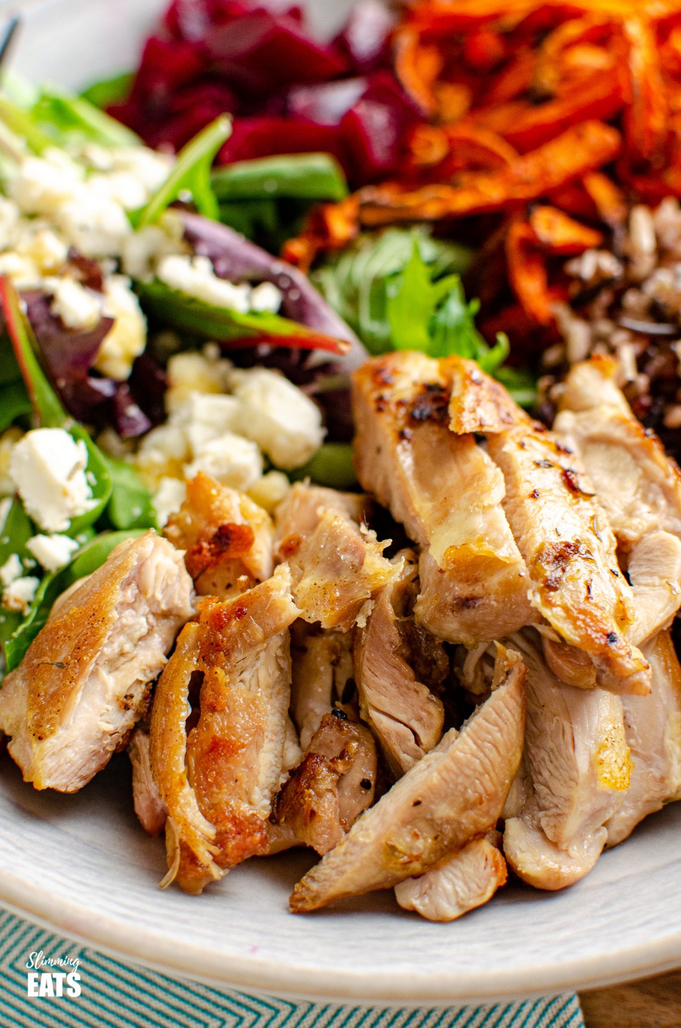 close up of Chicken Wild Rice Bowl - tender seasoned chicken thighs with a delicious nutty wild rice blend, roasted carrot strands, salad with beets and feta in a bowl 