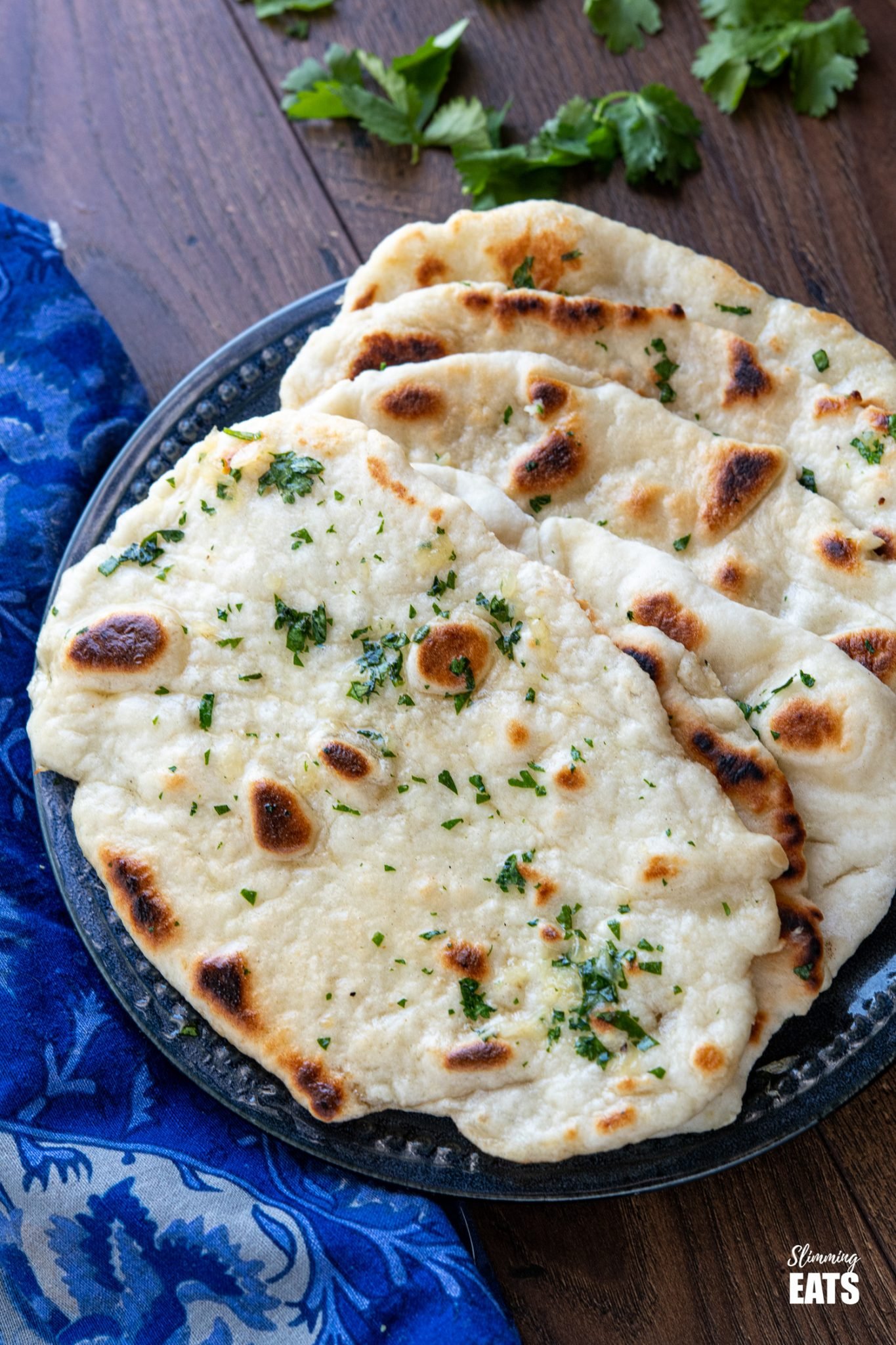 close up of Garlic Greek Yoghurt Naan Bread on dark blue plate with scattered cilantro