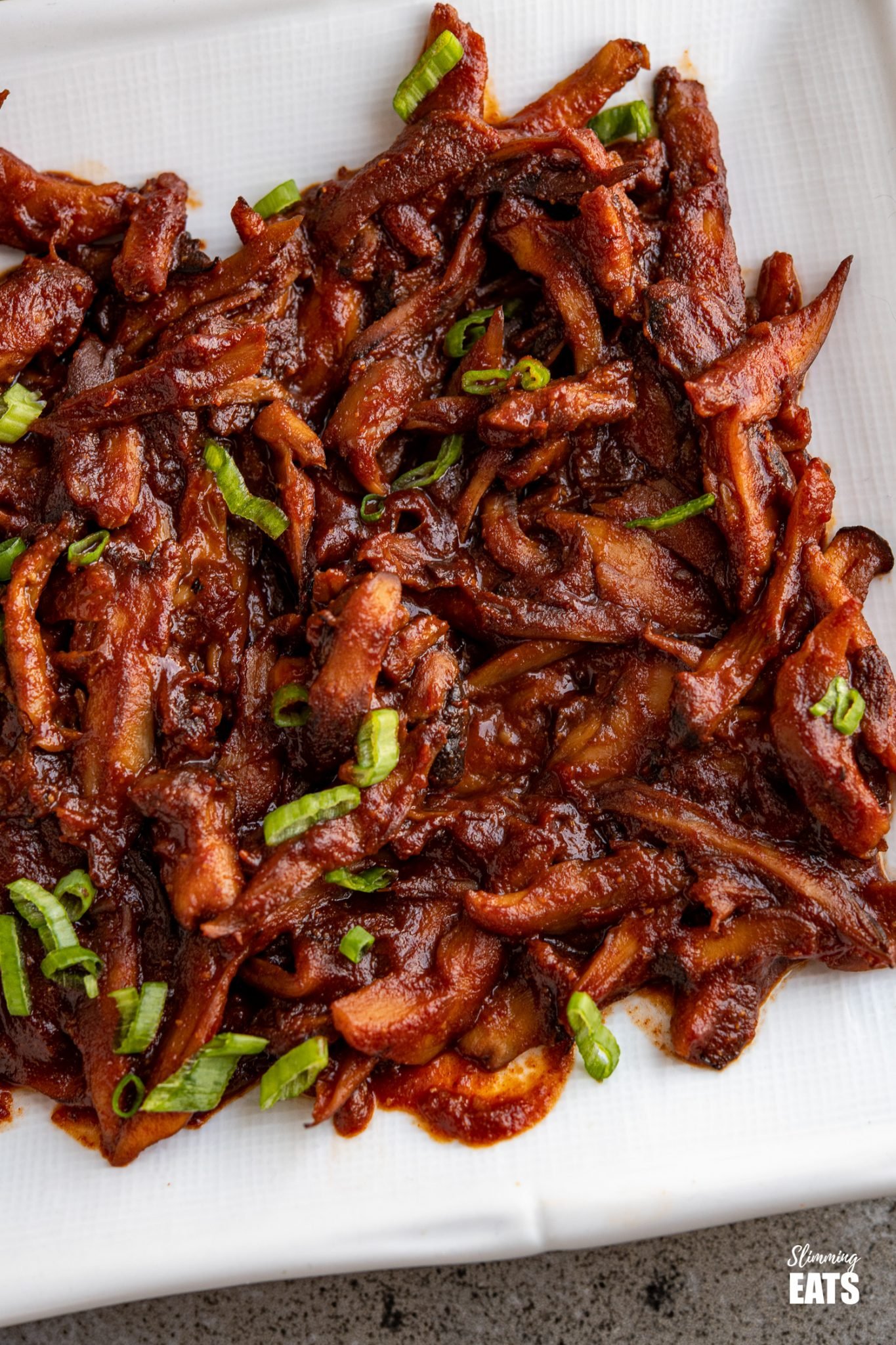 close up of Pulled Mushrooms with BBQ Sauce on white rectangle plate 