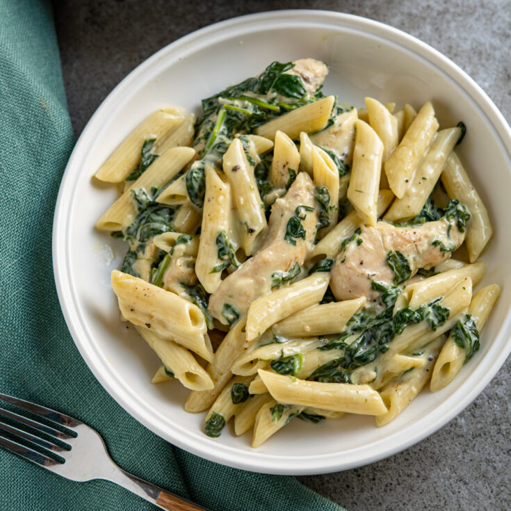 creamy garlic chicken spinach penne in a white bowl