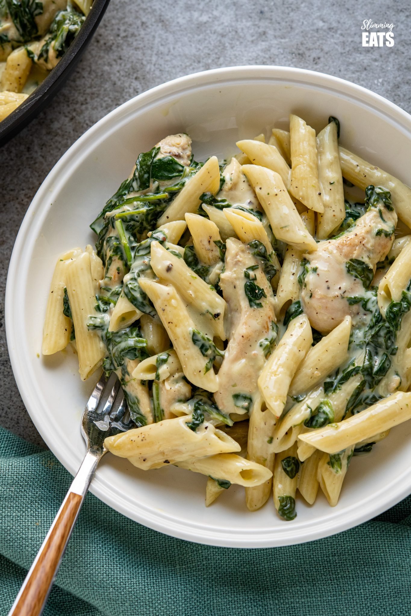 close up of creamy garlic chicken with spinach and penne pasta in white bowl