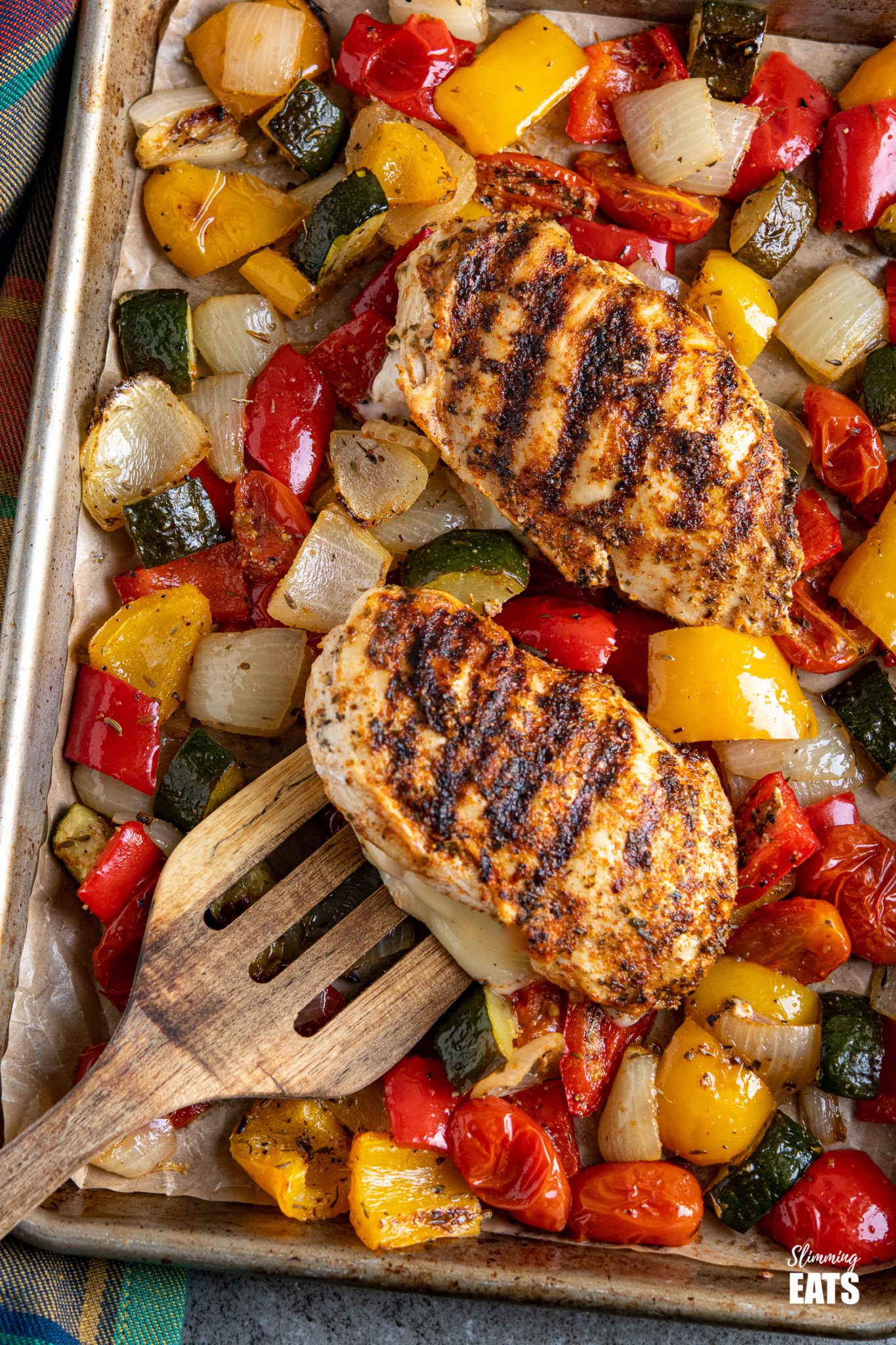 close up of grilled chicken stuffed with mozzarella and roasted vegetables on a baking tray line with parchment paper