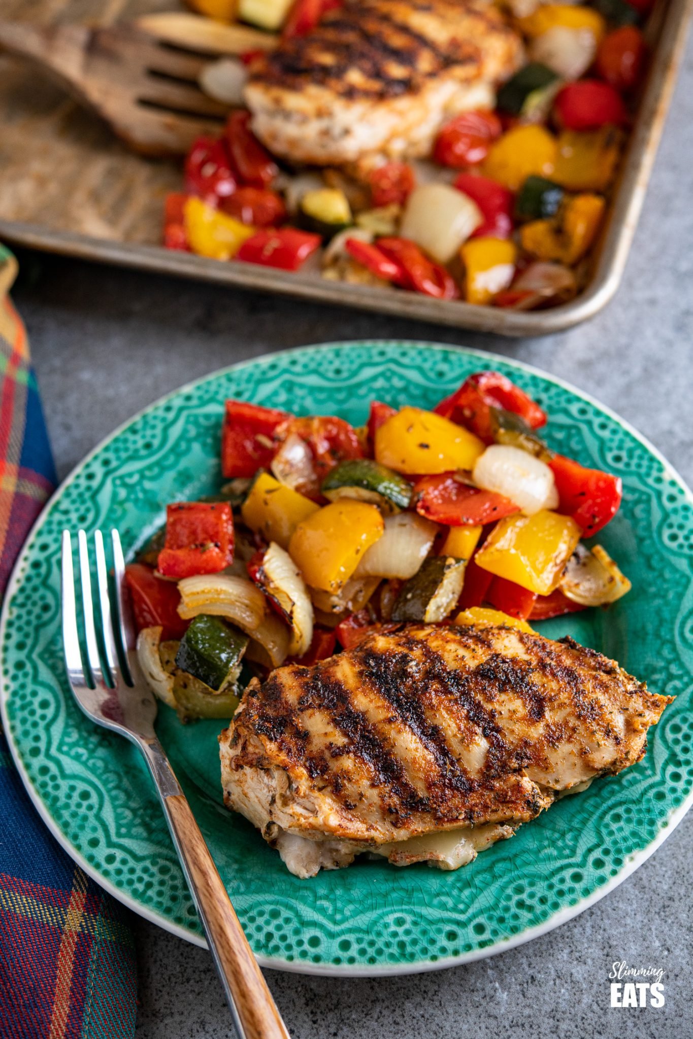 Simple seasoned Grilled Chicken Breast stuffed with mozzarella all delicious and melted served with a simple tray bake of roasted vegetables. #glutenfree #chicken #mozzarella #slimmingeats #weightwatchers #smartpoints #caloriecounting grilled chicken stuffed with mozzarella and roasted vegetables on a teal coloured plate with tray of roasted vegetables in background