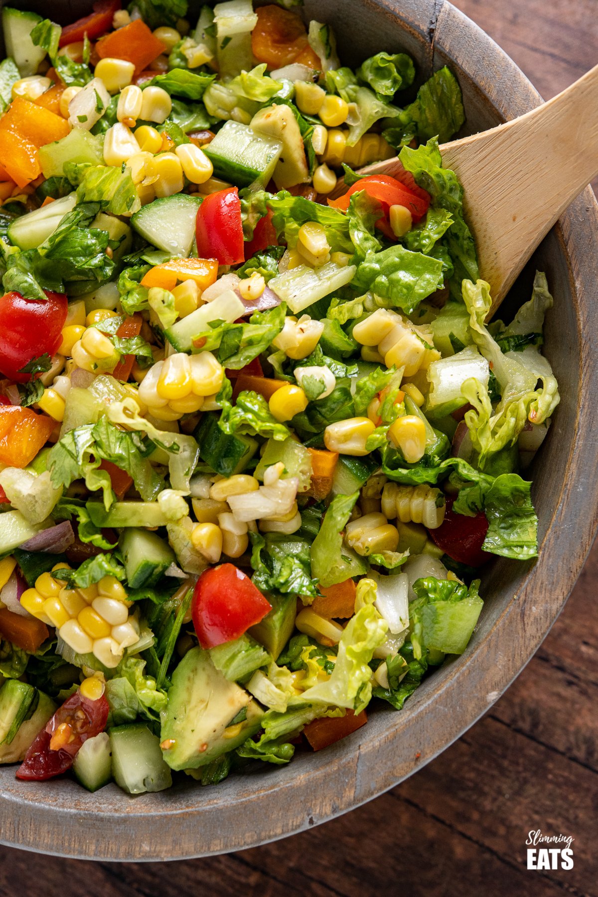 close up of chopped salad in wooden bowl with wooden spoon