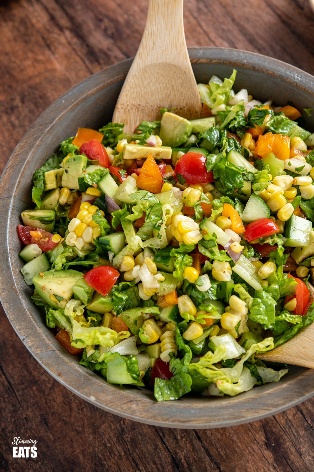 Mexican Chopped Salad - a perfect summertime salad that is great for barbecues with lettuce, tomatoes, peppers, onion, corn and avocado with a simple dressing. chopped salad in wooden bowl with wooden spoons