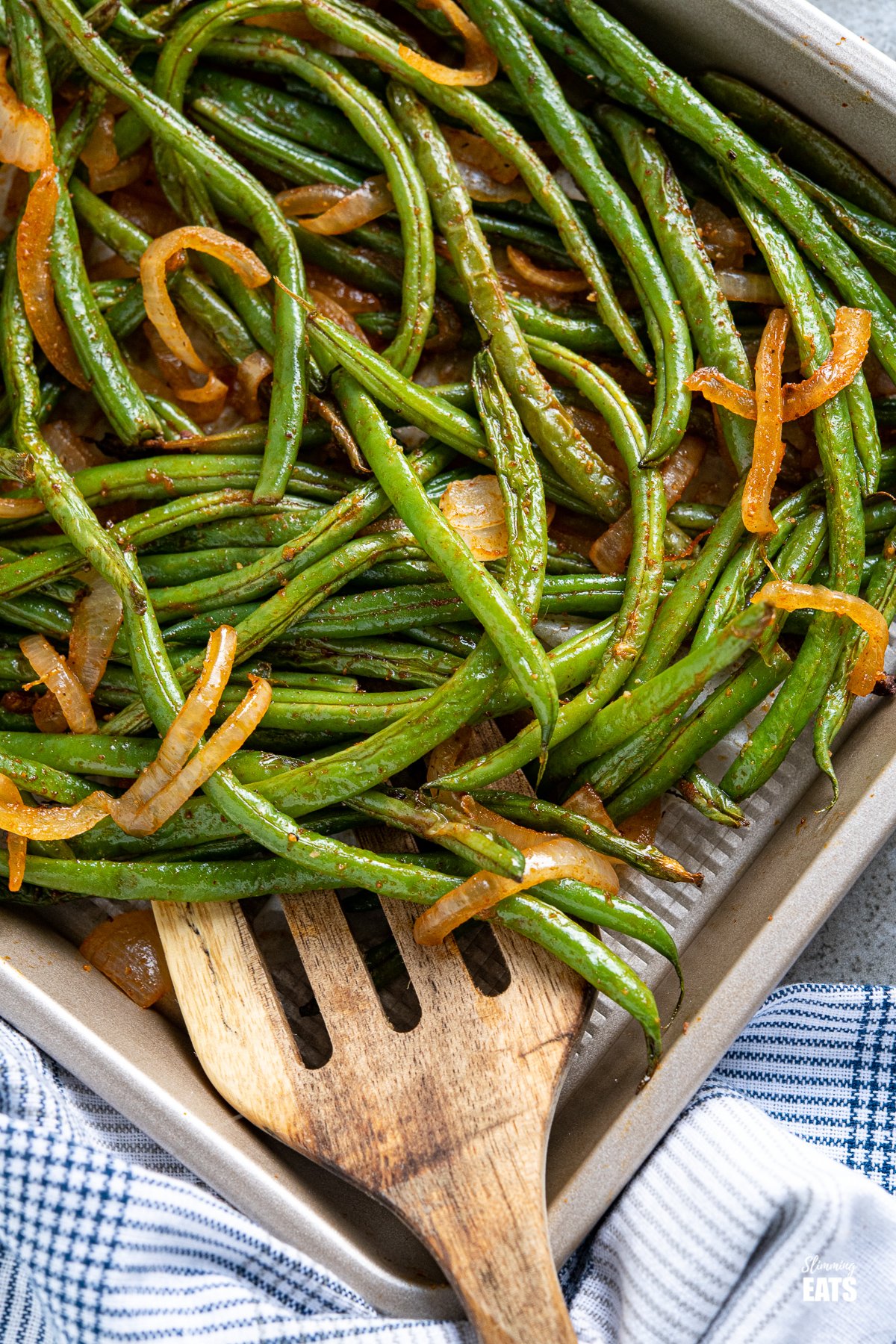 close up of Roasted Green Beans on a baking tray with wooden spatula