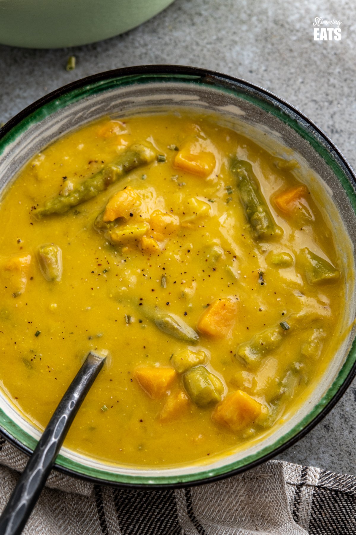 close up asparagus and sweet potato soup in white bowl with green, black and grey stripes, pan of soup in background