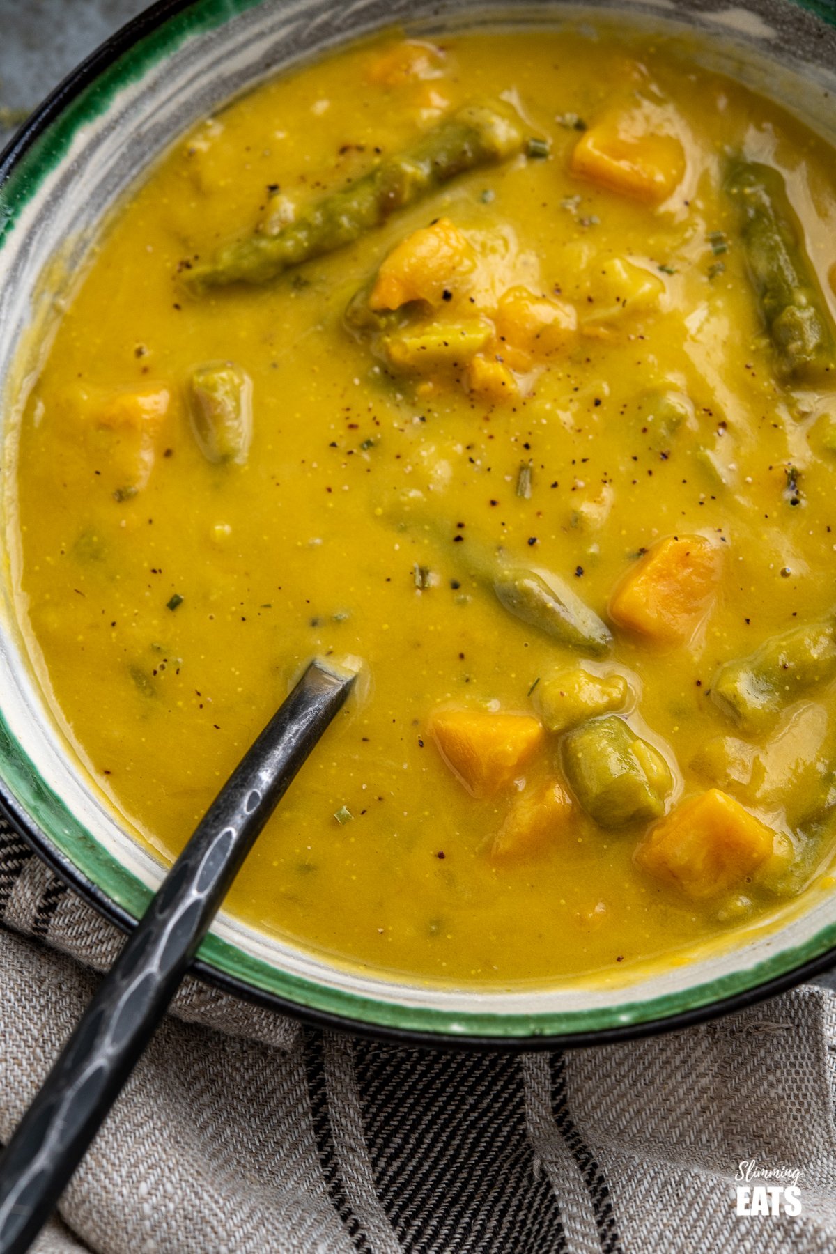 Asparagus and Sweet Potato Soup - delicious silky and creamy fresh asparagus soup with a subtle sweetness from cubes of sweet potato - pure comfort in a bowl. #glutenfree #dairyfree #slimmingworld #weightwatchers close up asparagus sweet potato soup in white bowl with green, black and grey stripes
