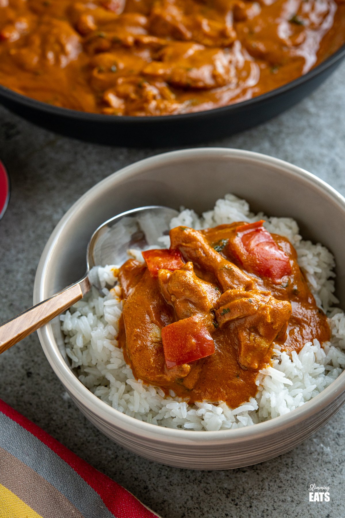 Coconut Chicken and Red Pepper Curry - a delicious curry with tender pieces of chicken in a thick creamy red pepper curry sauce. chicken curry in a grey bowl with white rice and a wooden handled spoon placed in the left hand side of the bowl