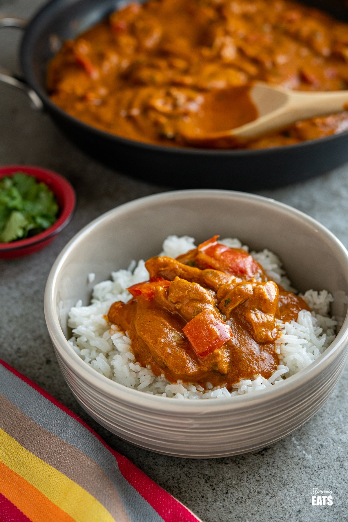 chicken curry in a grey bowl with white rice with a frying pan in the background 