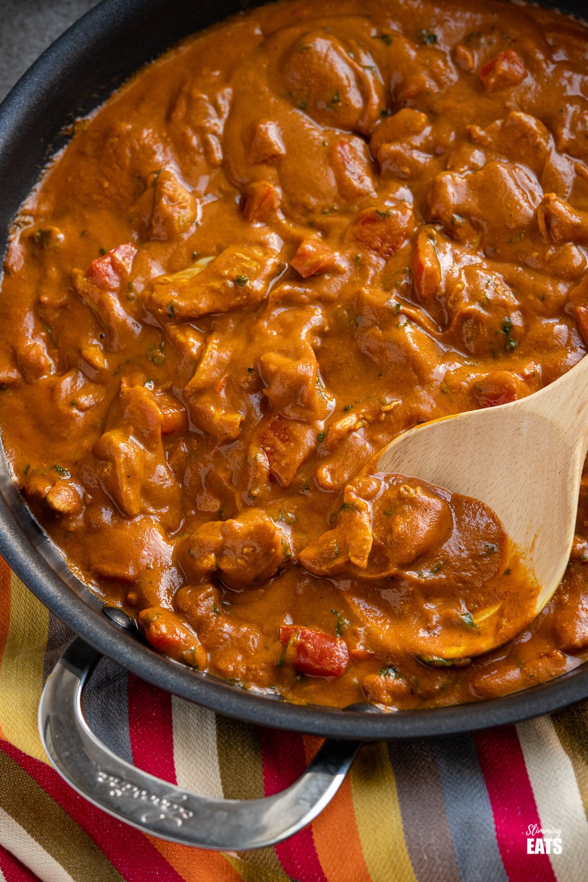 close up of chicken curry in a black frying pan with wooden spoon