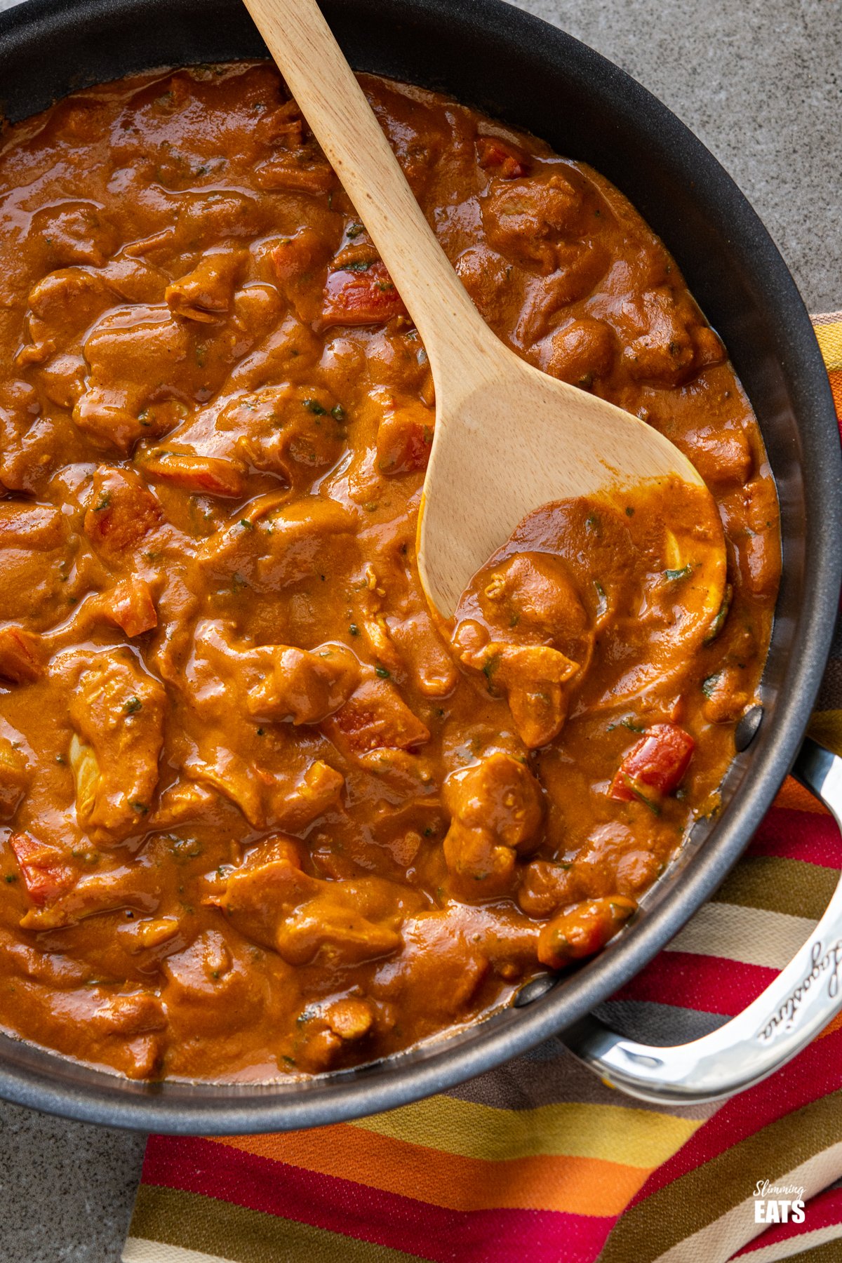 close up of chicken curry in black frying pan with wooden spoon