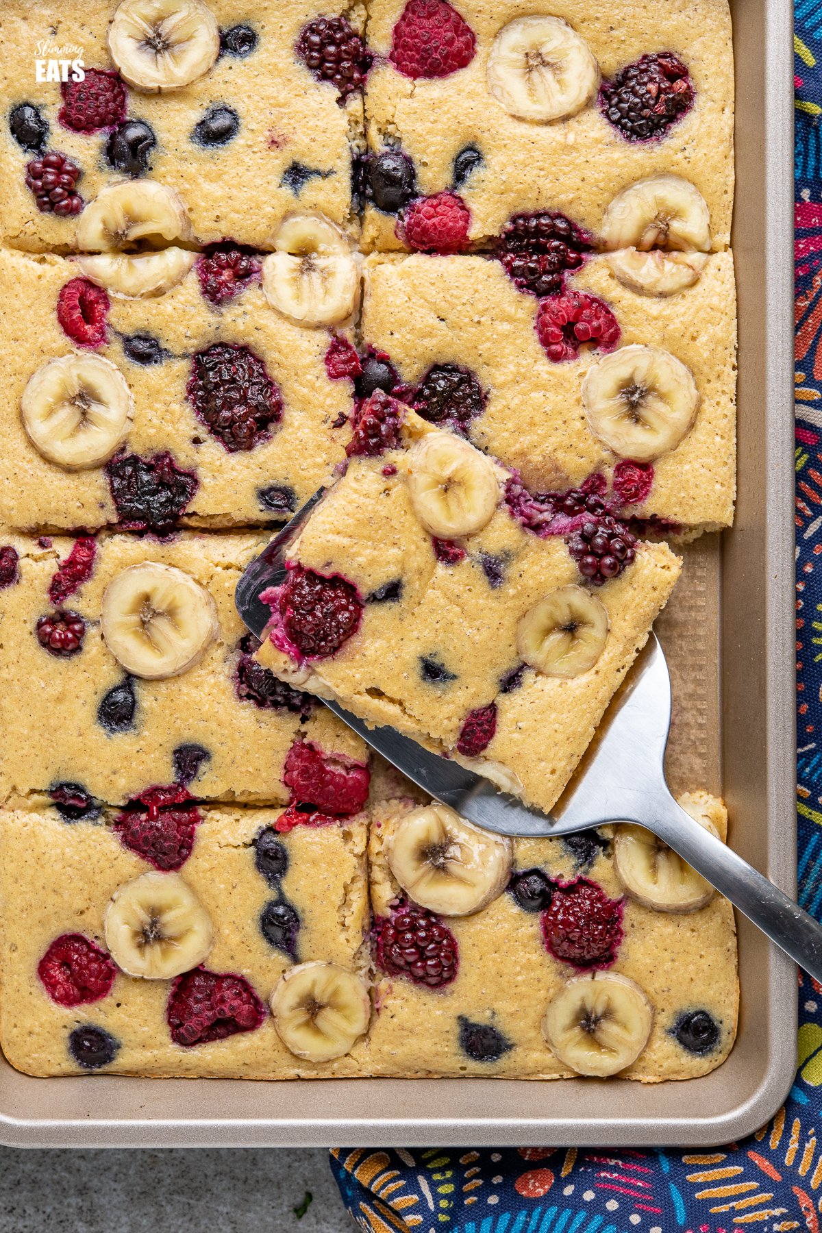 Sheet Pan Oat Pancakes - love pancakes but hate the flipping and standing at the stove? These easy sheet pan oat pancakes with berries and banana is the perfect effortless breakfast. Slimming World and Weight Watchers friendly close up of sliced Sheet Pan Oat Pancakes in a baking tray with spatula
