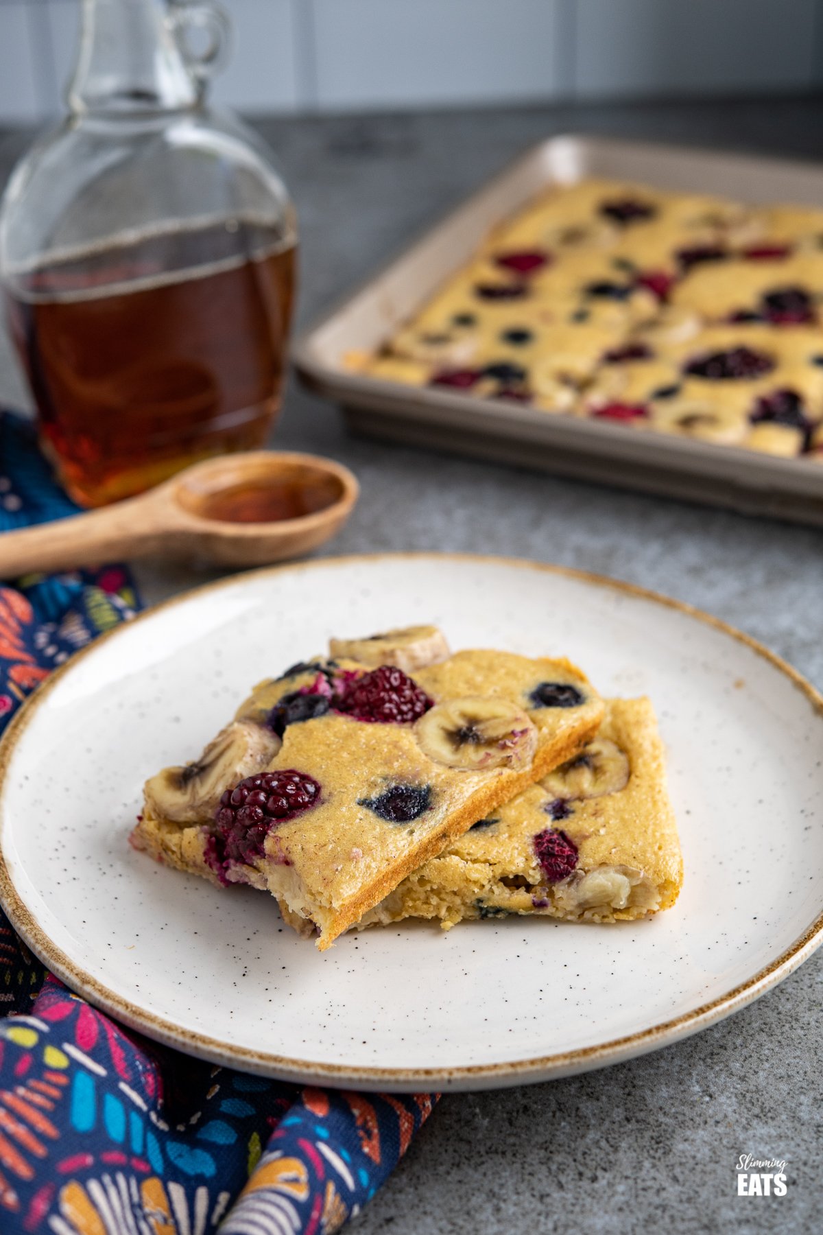 Sheet Pan Oat Pancakes on a white plate with cream rim, maple syrup and sheet pan in background