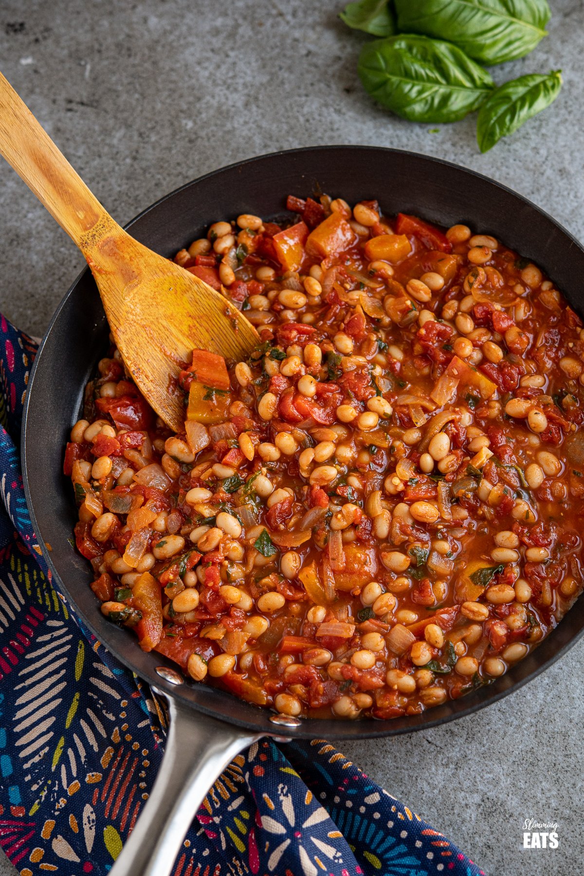 Tomatoes and White Beans in a black frying pan with a bunch of fresh basil in top right corner. 