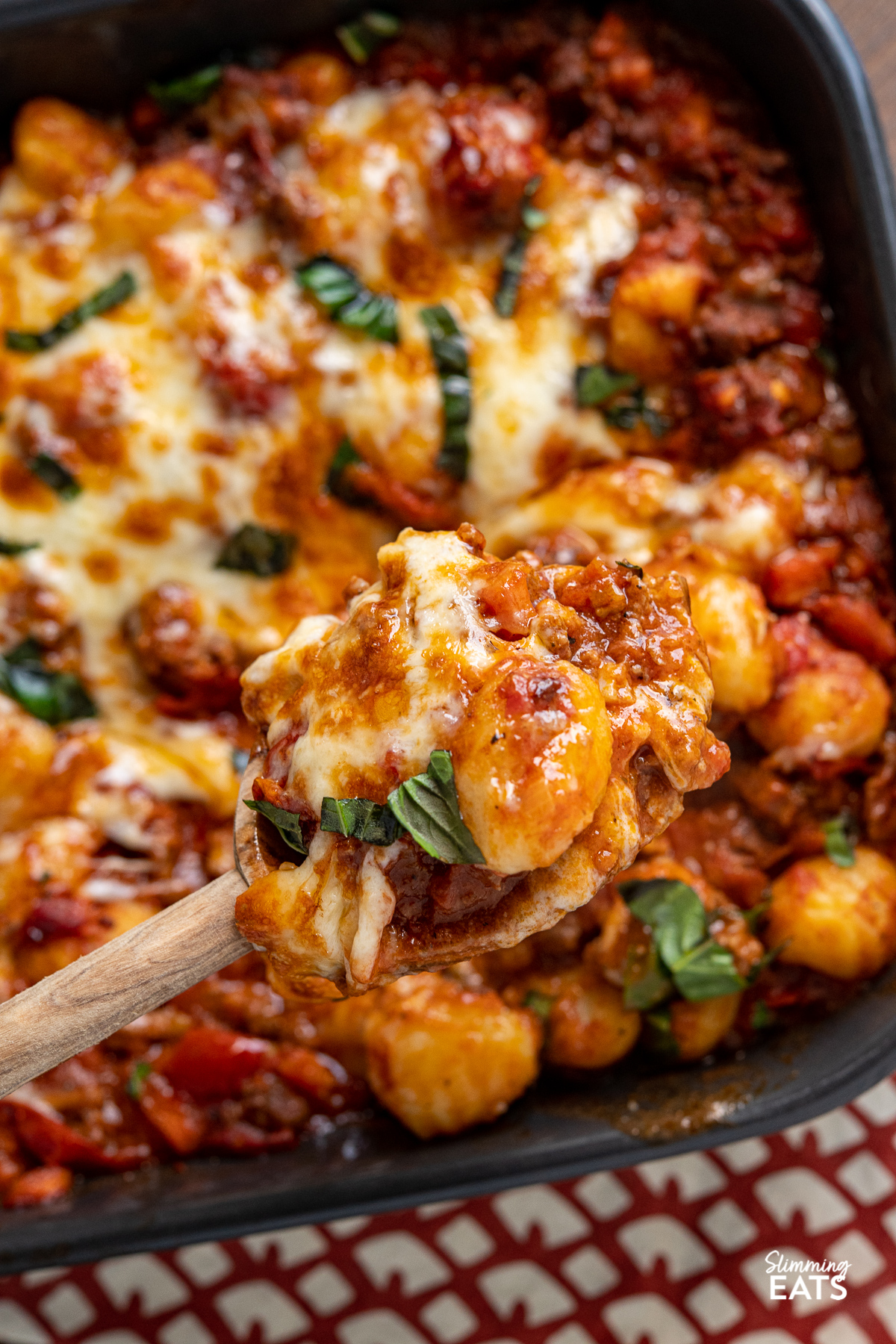 cheesy bolognese meat and gnocchi being spooned out of grey baking dish 