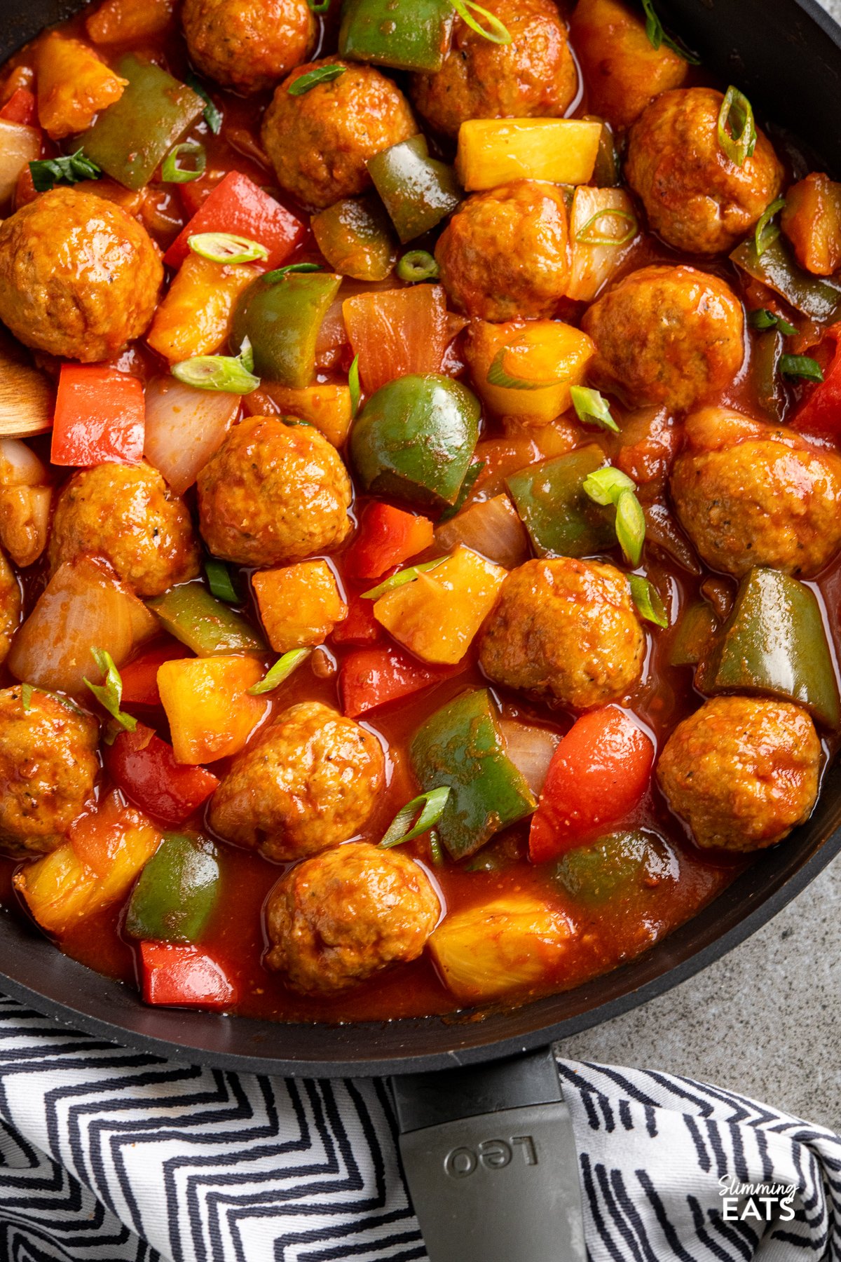 close up of sweet and sour chicken meatballs in black frying pan with vegetables and pineapple