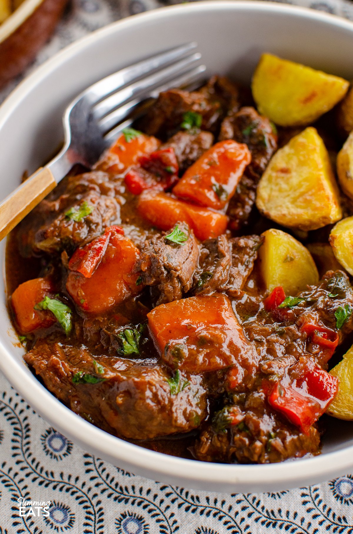This delicious bowl of Balsamic Braised Beef is pure comfort food. Tender chunks of beef in a tangy rich tomato sauce. Gluten free, dairy free, Slimming World and Weight Watchers friendly close up of grey bowl of balsamic braised beef with fork place to side
