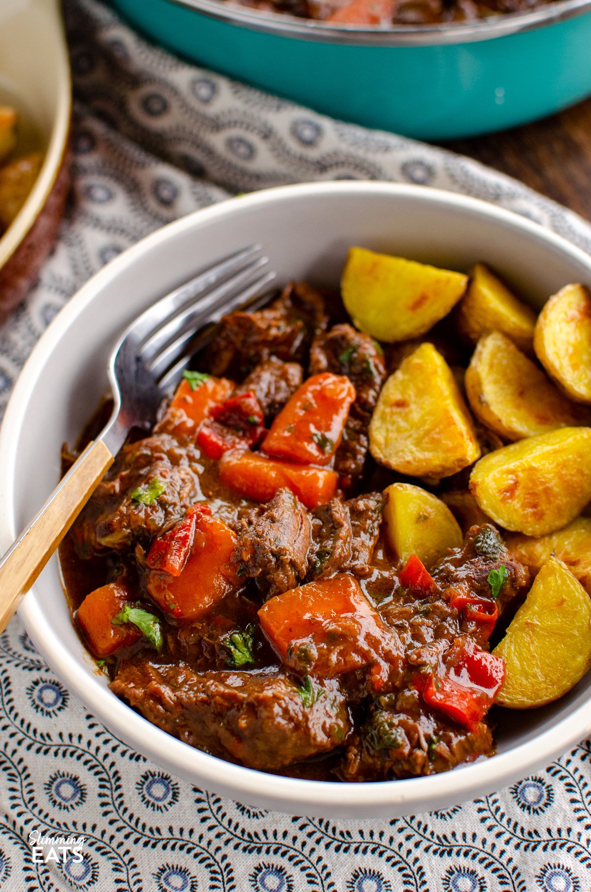 grey bowl of balsamic braised beef with roasted Yukon gold potatoes on a patterned placemat