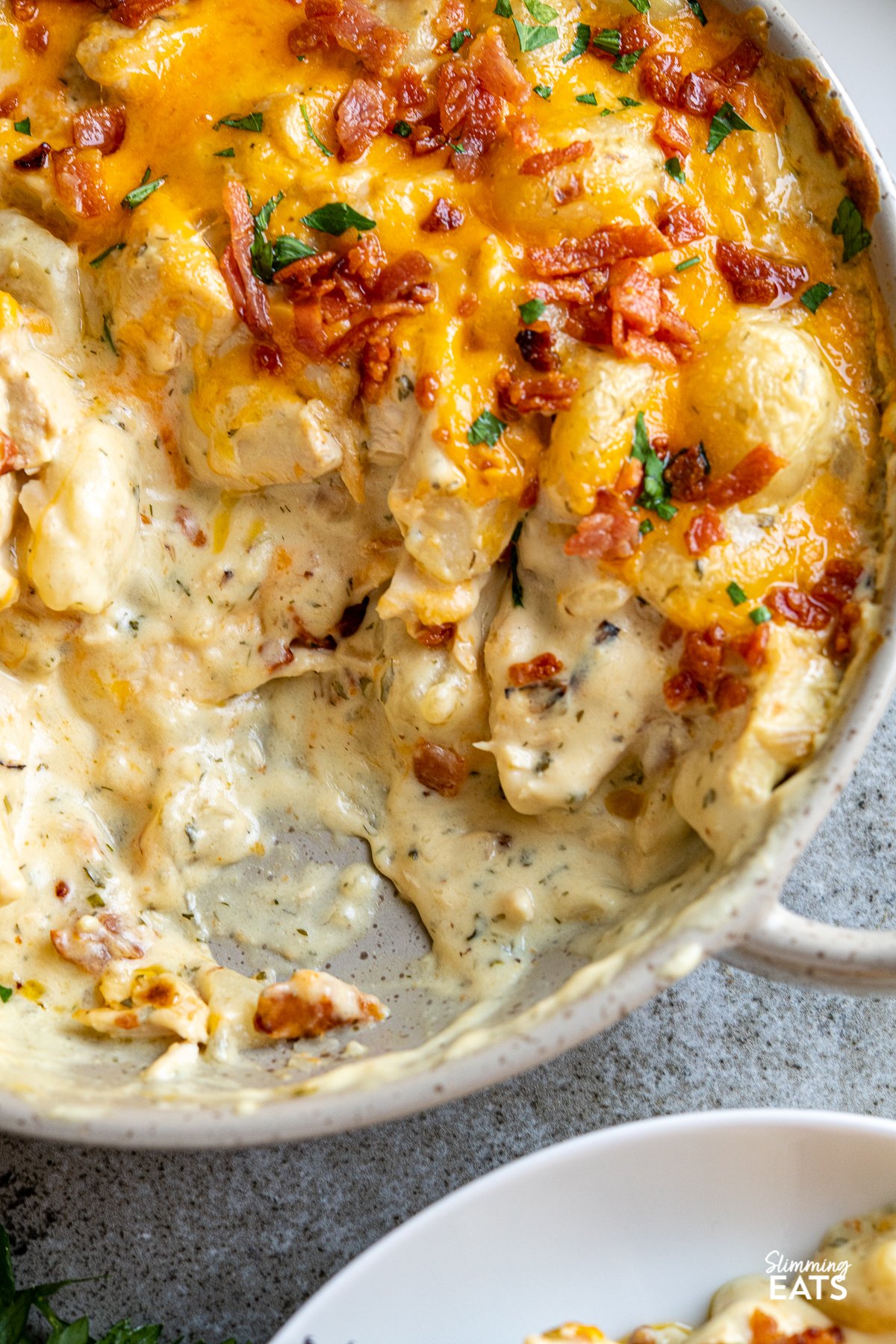 close up of crack chicken gnocchi  in double handled grey brown ceramic dish with melted cheddar and crisp golden bacon.