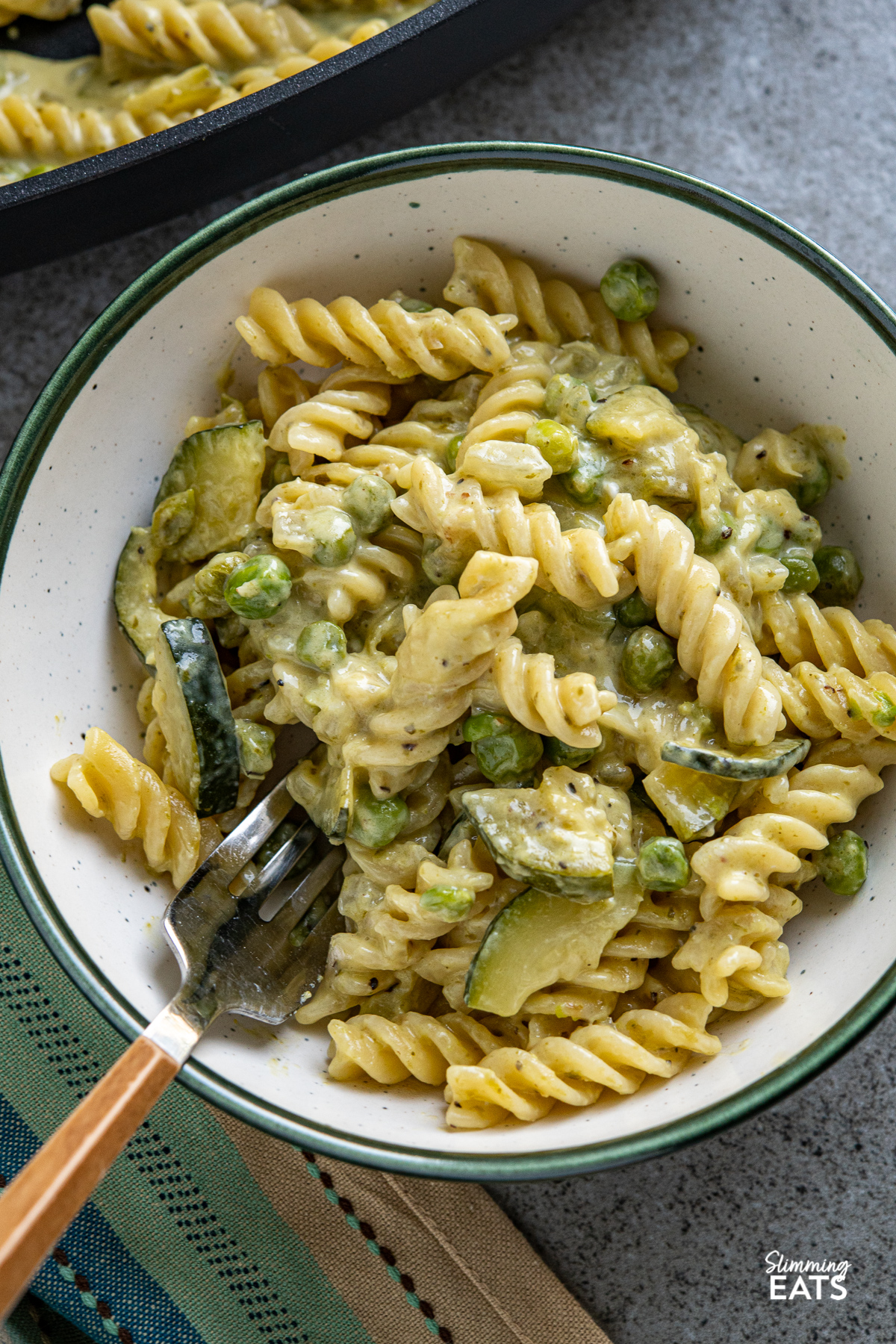 close up of serving of One Pot Creamy Pesto Courgette Pea Pasta in white bowl with dark green rim