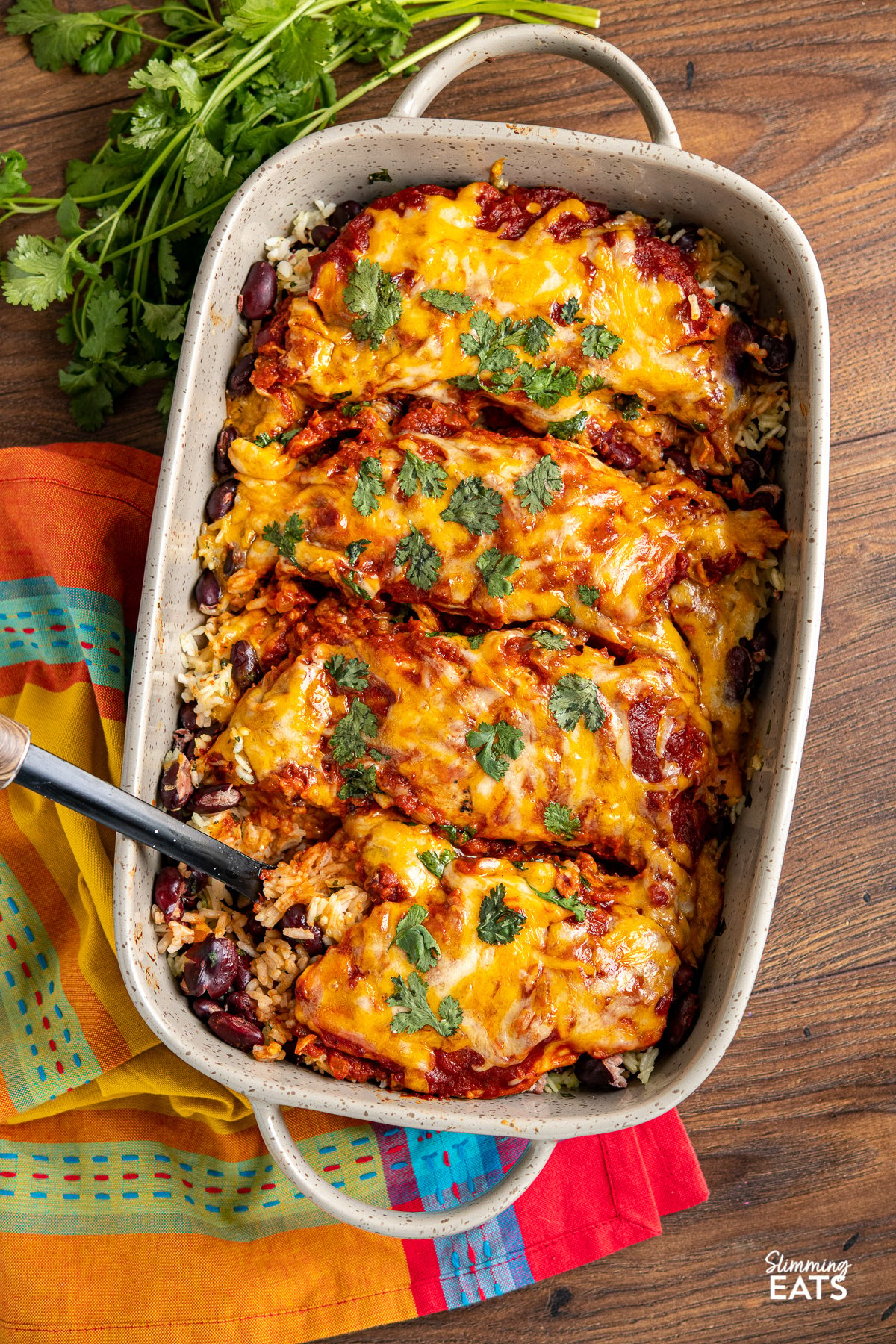 Mexican Chicken and Rice Bake in brown grey ceramic baking dish with two handles placed on a bright colour towel on wooden surface