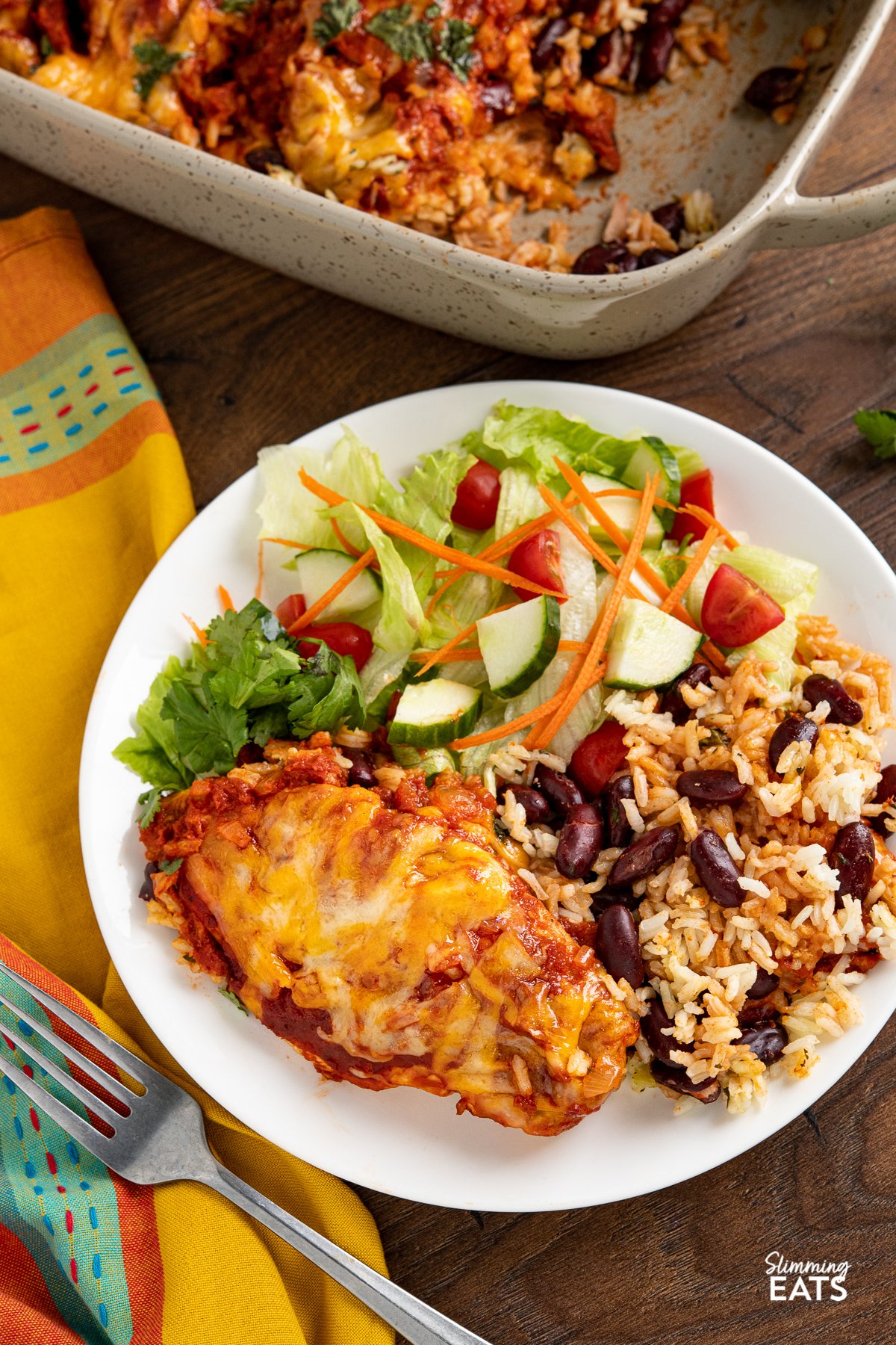 serving of Mexican Chicken and Rice Bake on a white plate with a mixed salad of lettuce, tomatoes, cucumber and carrot.