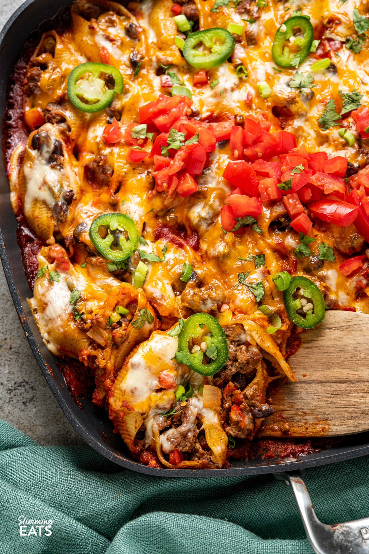 close up  of Cheesy Beef Enchilada Stuffed Pasta Shells in all-clad skillet with wooden spatula placed in pan