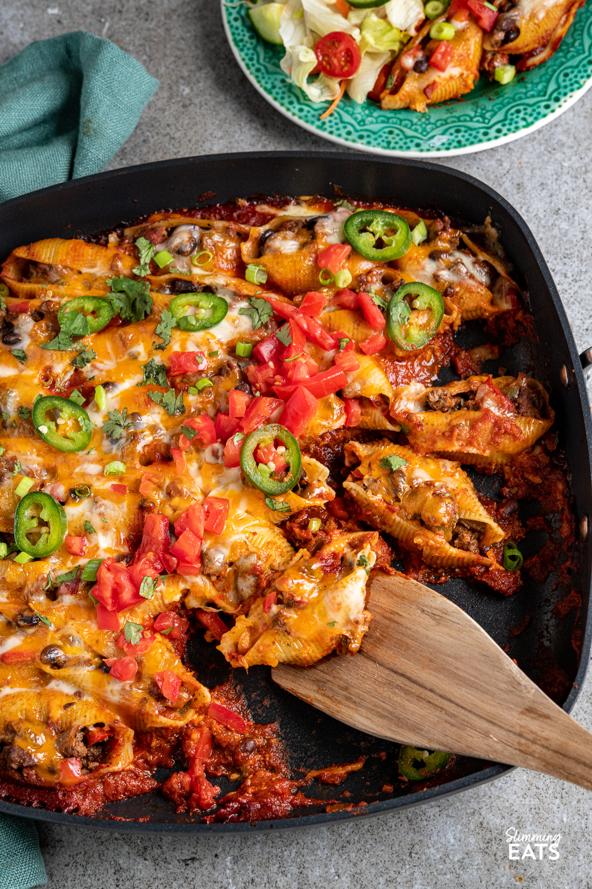 Cheesy Beef Enchilada Stuffed Pasta Shells in all-clad skillet with wooden spatula placed in pan