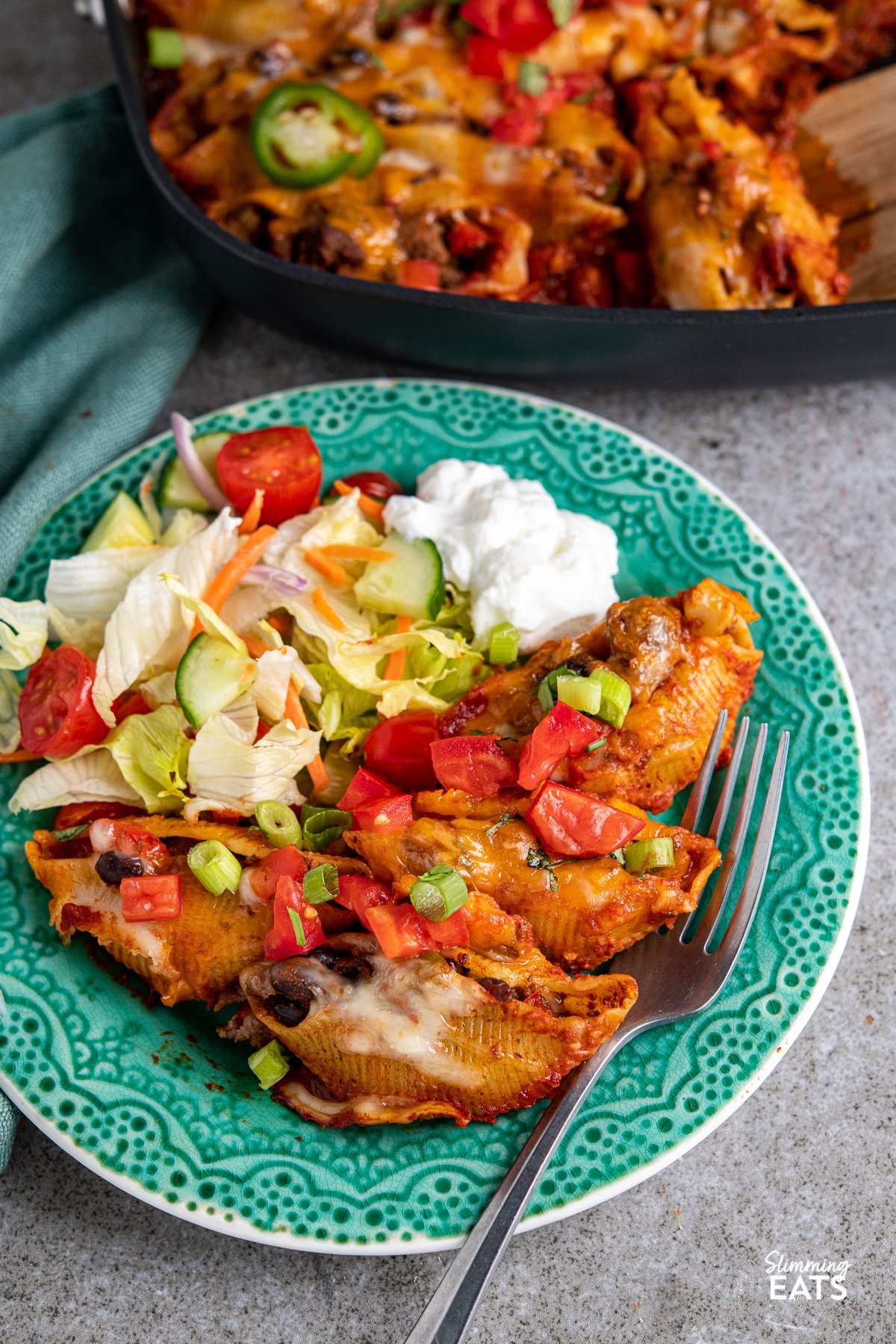 Cheesy Beef Enchilada Stuffed Pasta Shells on a turquoise patterned plate with salad and sour cream