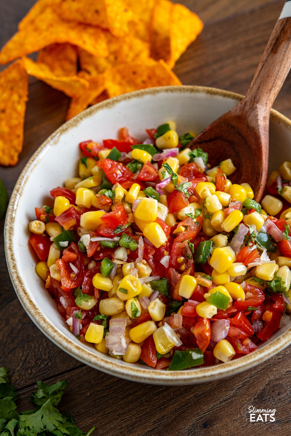 Easy Corn and Tomato Salsa in white bowl with light brown rim and wooden spoon