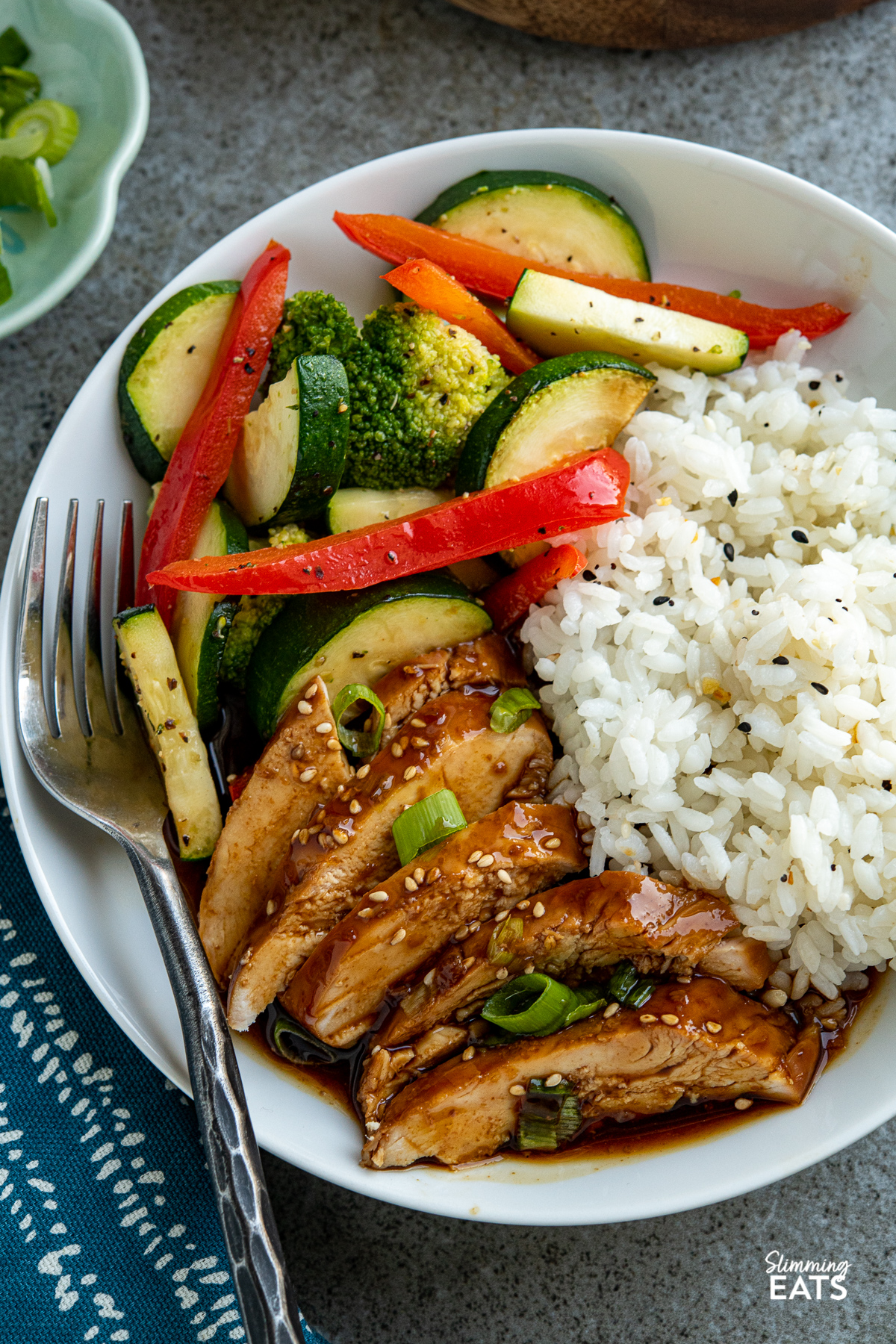 close up of sliced Slow Cooker Teriyaki Chicken on white plate with rice and stir fried red pepper, zucchini and broccoli