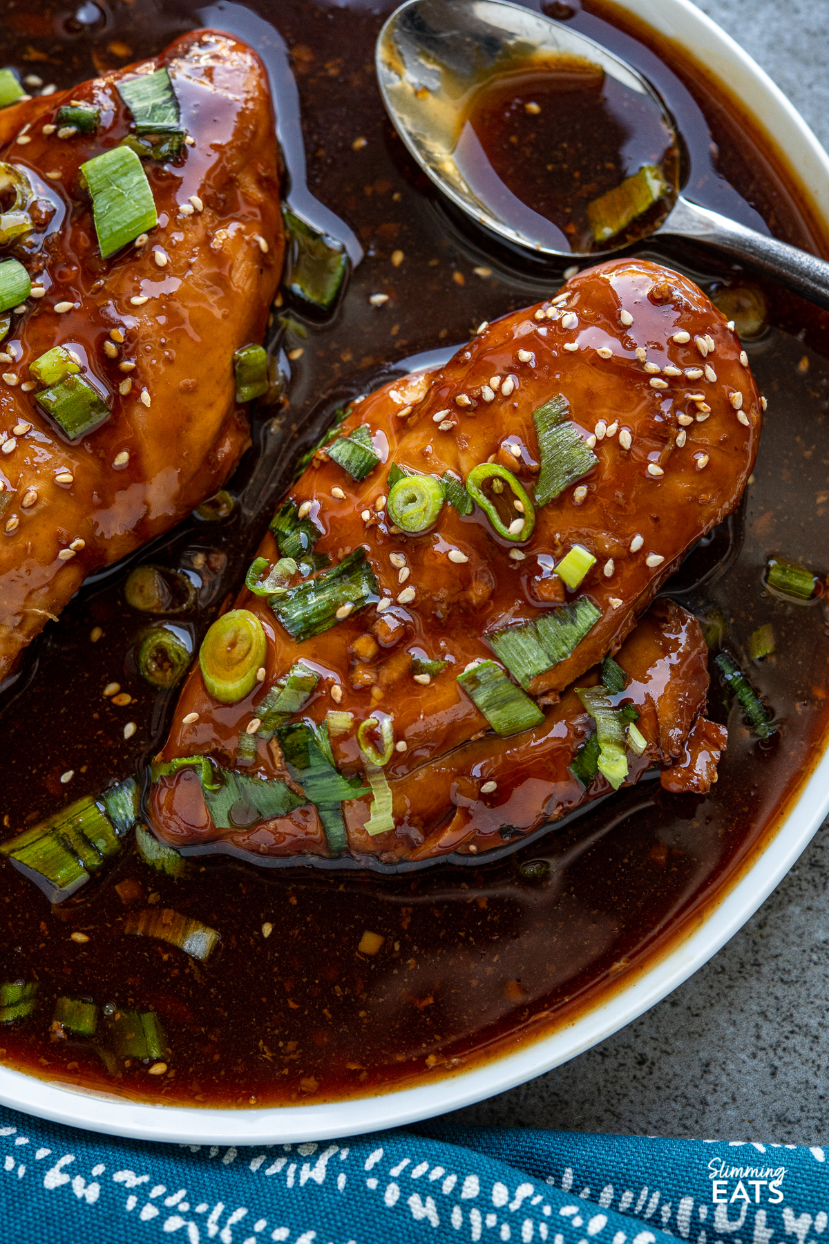 close up of Slow Cooker Teriyaki Chicken on white plate with scattered spring onions and sesame seeds.