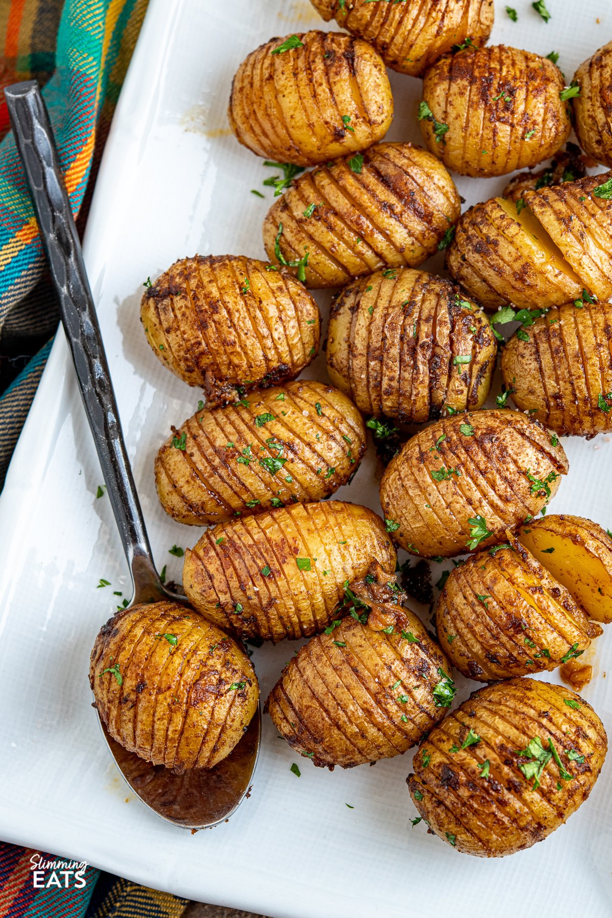Garlic Hasselback Potatoes are one of the best kind of baked potato you will ever make, the buttery garlic melts perfectly into all the thin slices in the potato adding heaps of flavour. Vegetarian, Slimming Eats and Weight Watchers friendly Garlic Hasselback Potatoes on a white plate with metal spoon