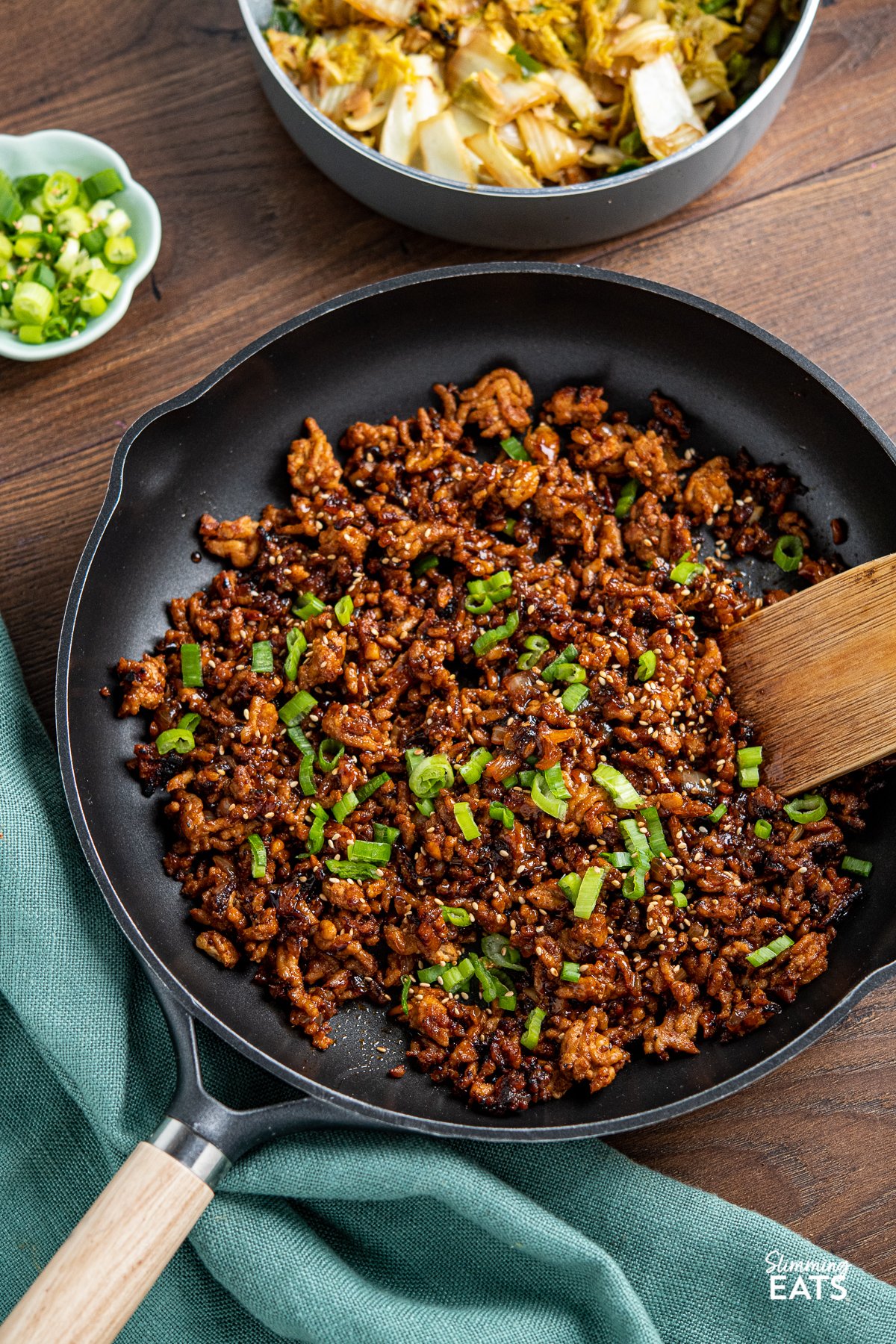 Delicious Korean Ground Pork in a black frying pan with wooden handle, scattered spring onions and sesame seeds