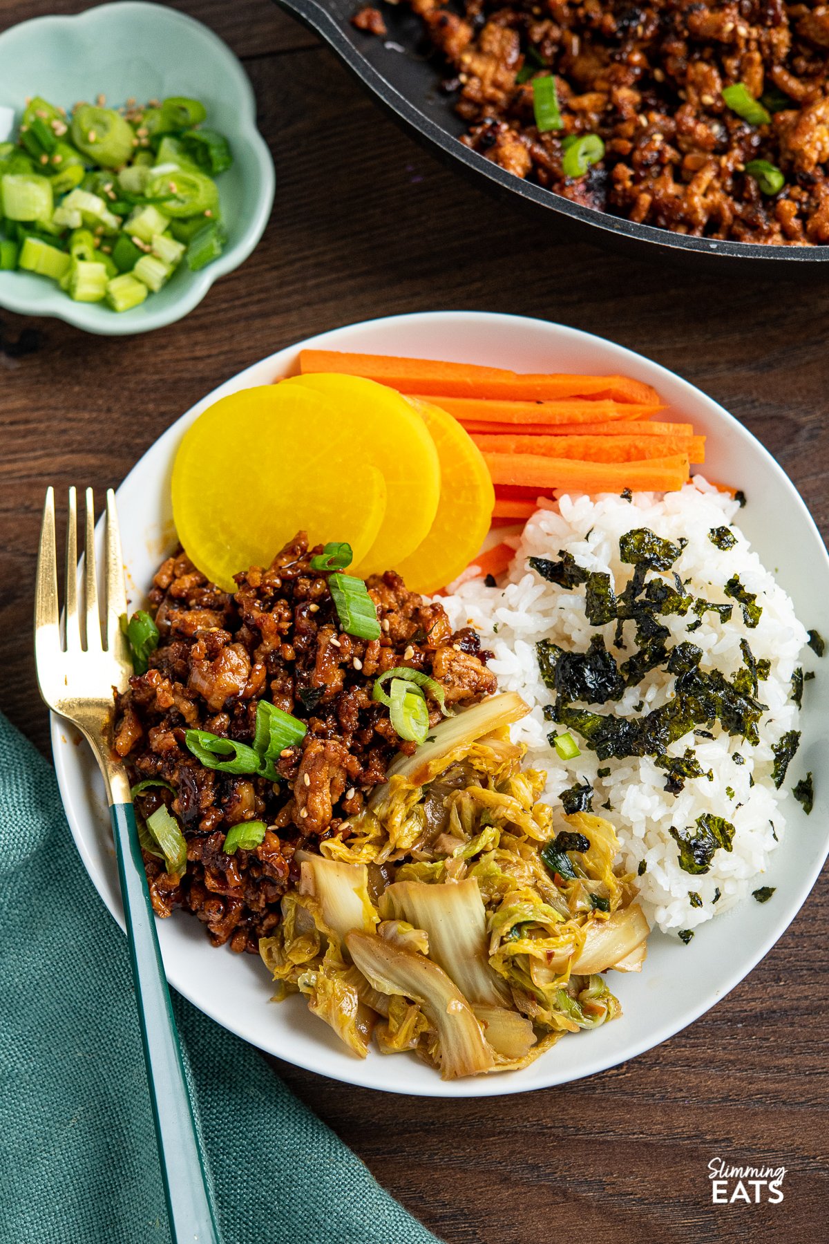 Delicious Korean Ground Pork in a white bowl with rice, carrots, daikon radish, garlic cabbage and nori seaweed