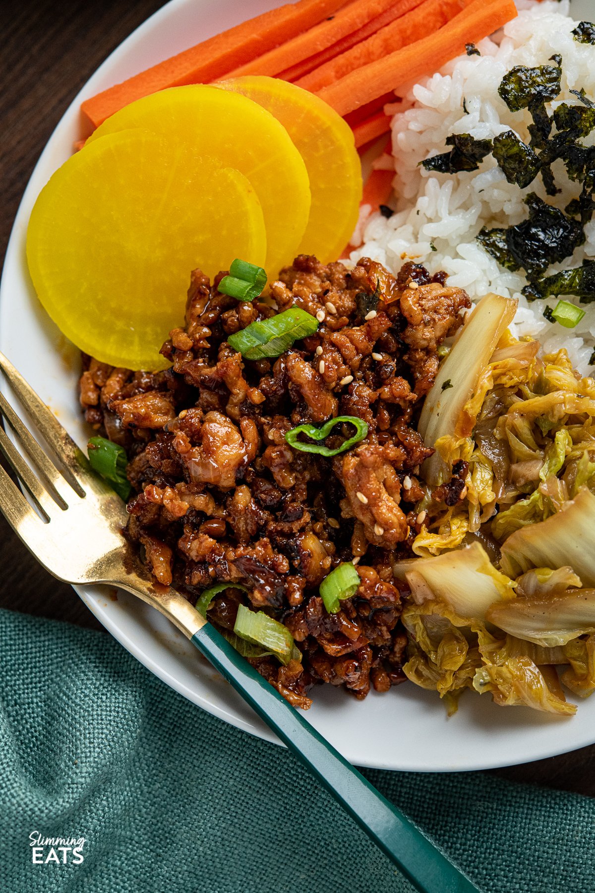 close up of Delicious Korean Ground Pork in a white bowl with rice, carrots, daikon radish, garlic cabbage and nori seaweed