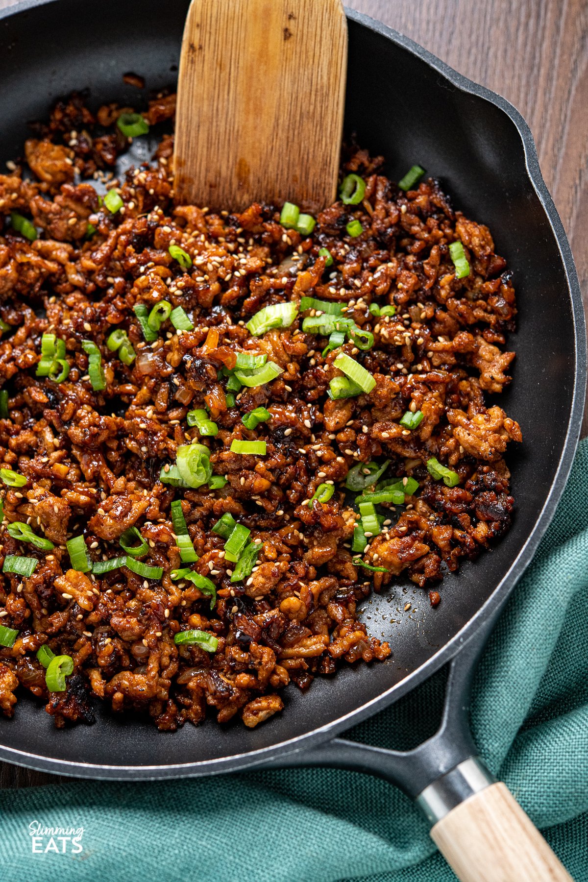 close up of Delicious Korean Ground Pork in a black frying pan with wooden handle, scattered spring onions and sesame seeds