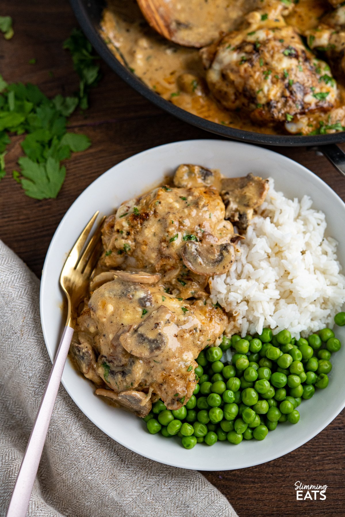 white bowl with serving of smothered garlic chicken with white rice and green peas, fork place to left in bowl. 