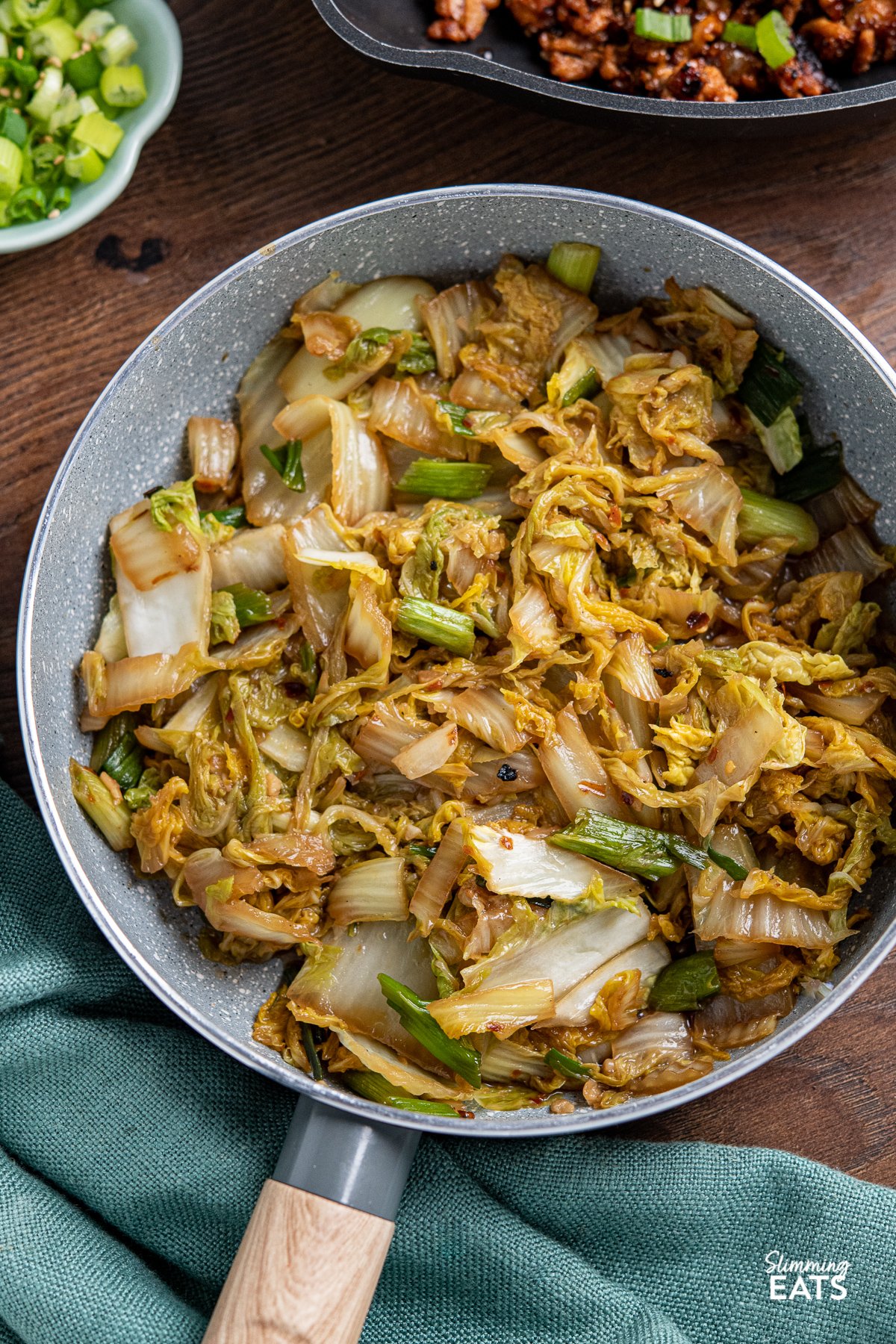 Spicy Garlic Napa Cabbage in grey frying pan with wooden handle, pan of Korean ground pork in background