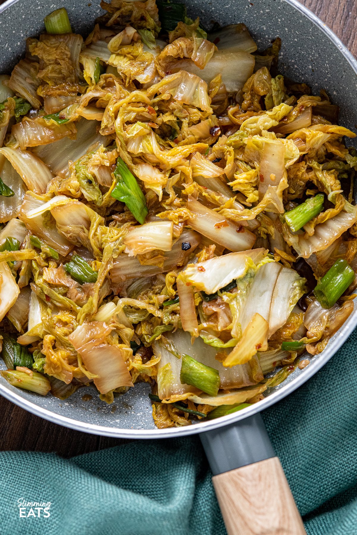 Spicy Garlic Napa Cabbage - delicious pan fried Napa cabbage with fresh garlic and the spicy kick from red chilli flakes. A perfect side for a variety of main dishes. Slimming World and Weight Watchers friendly close up of Spicy Garlic Napa Cabbage in grey frying pan with wooden handle