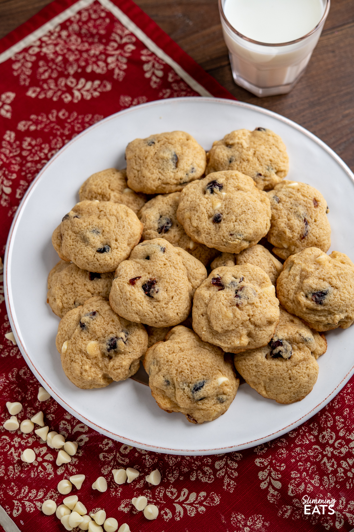 pile of Cranberry White Chocolate Scone Cookies on a round white plate with glass of milk behind