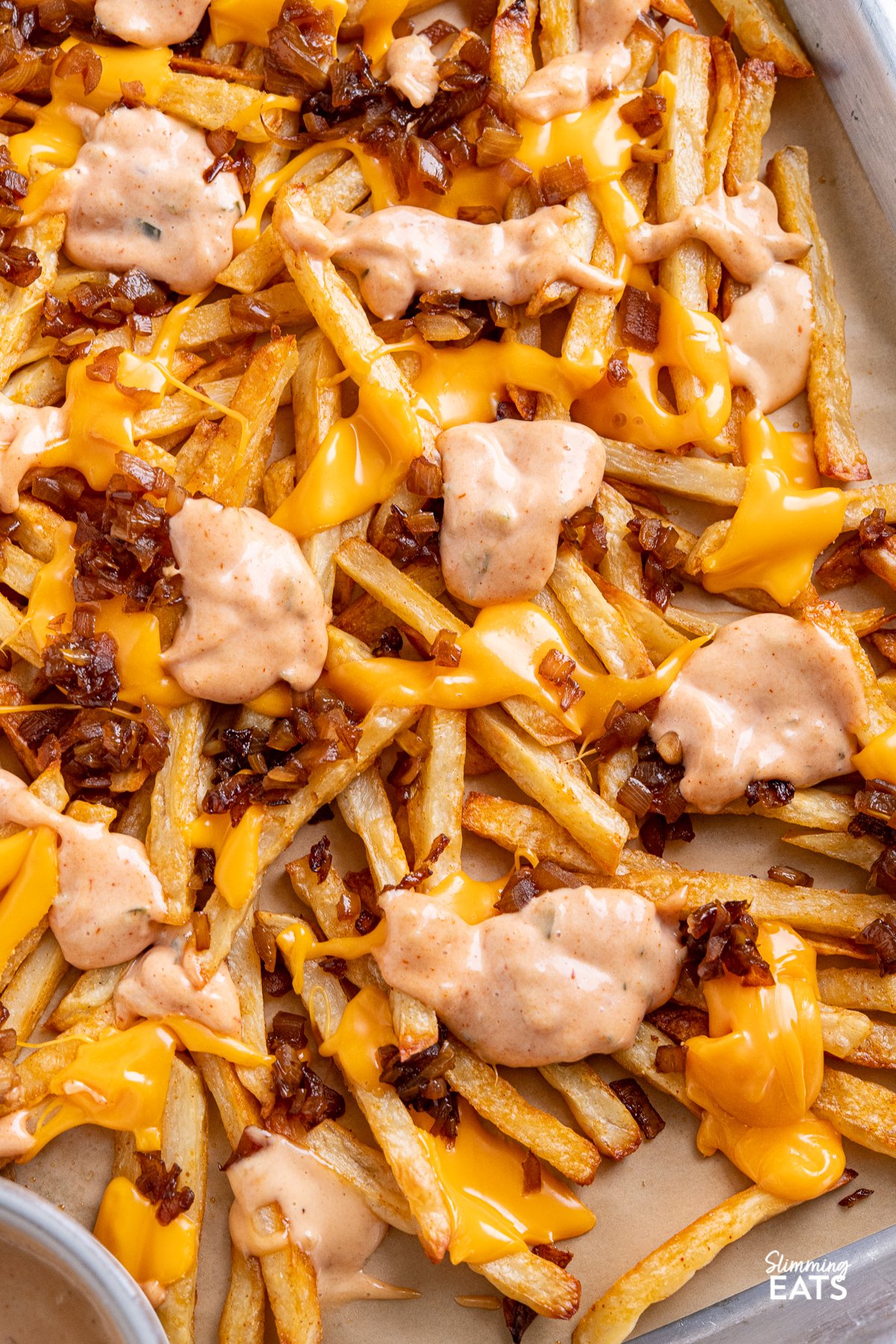 Indulge with these classic fakeaway Animal Style Fries - sweet sauteed onions, golden oven baked fries with melted American cheese and a classic special sauce what more could one want? close up of Copycat Oven Baked Animal Style Fries on a baking tray